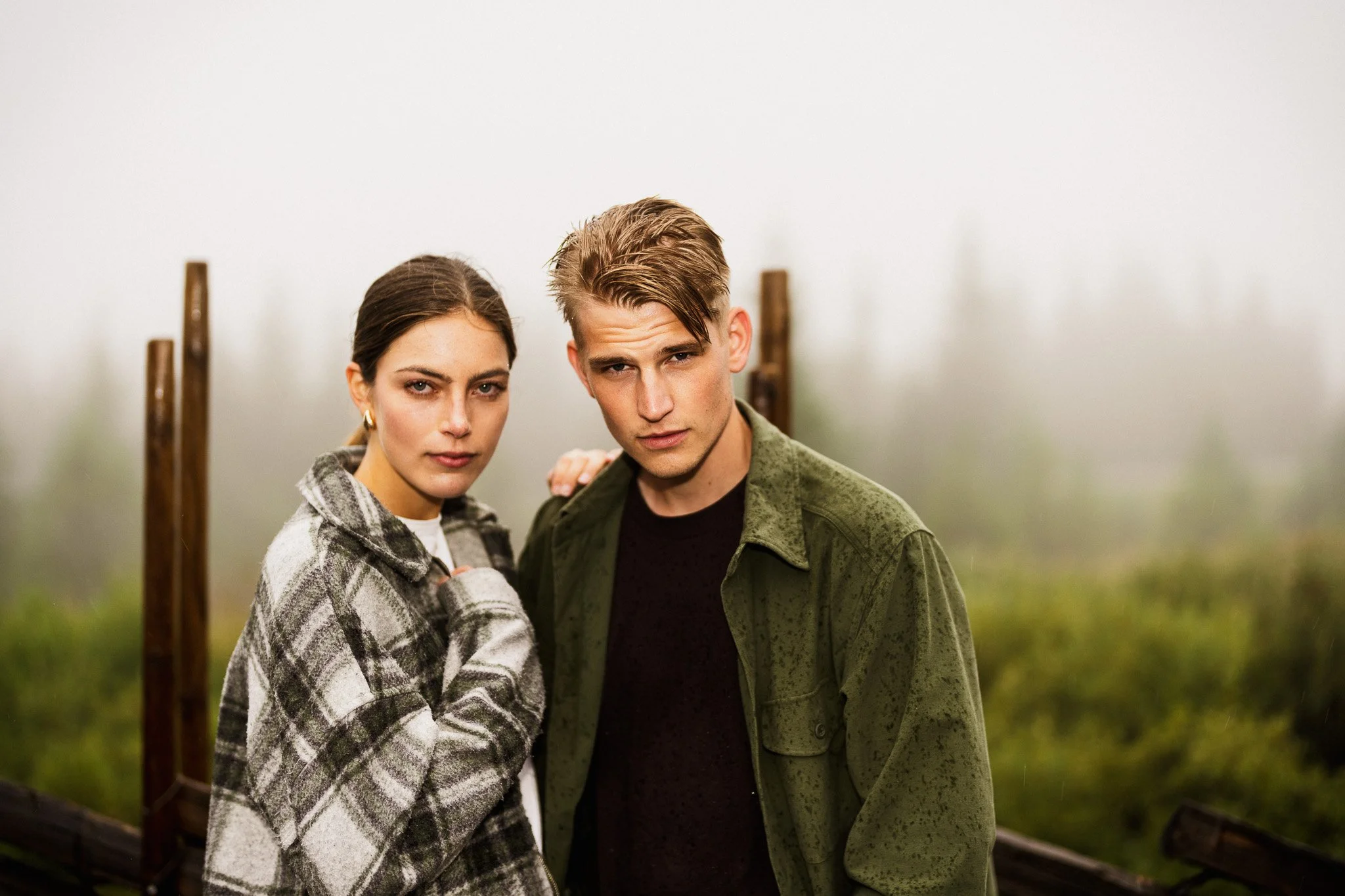 En ung man och en ung kvinna står nära varandra utomhus, med dimmig och grönskande natur i bakgrunden, båda riktar blickarna mot kameran.