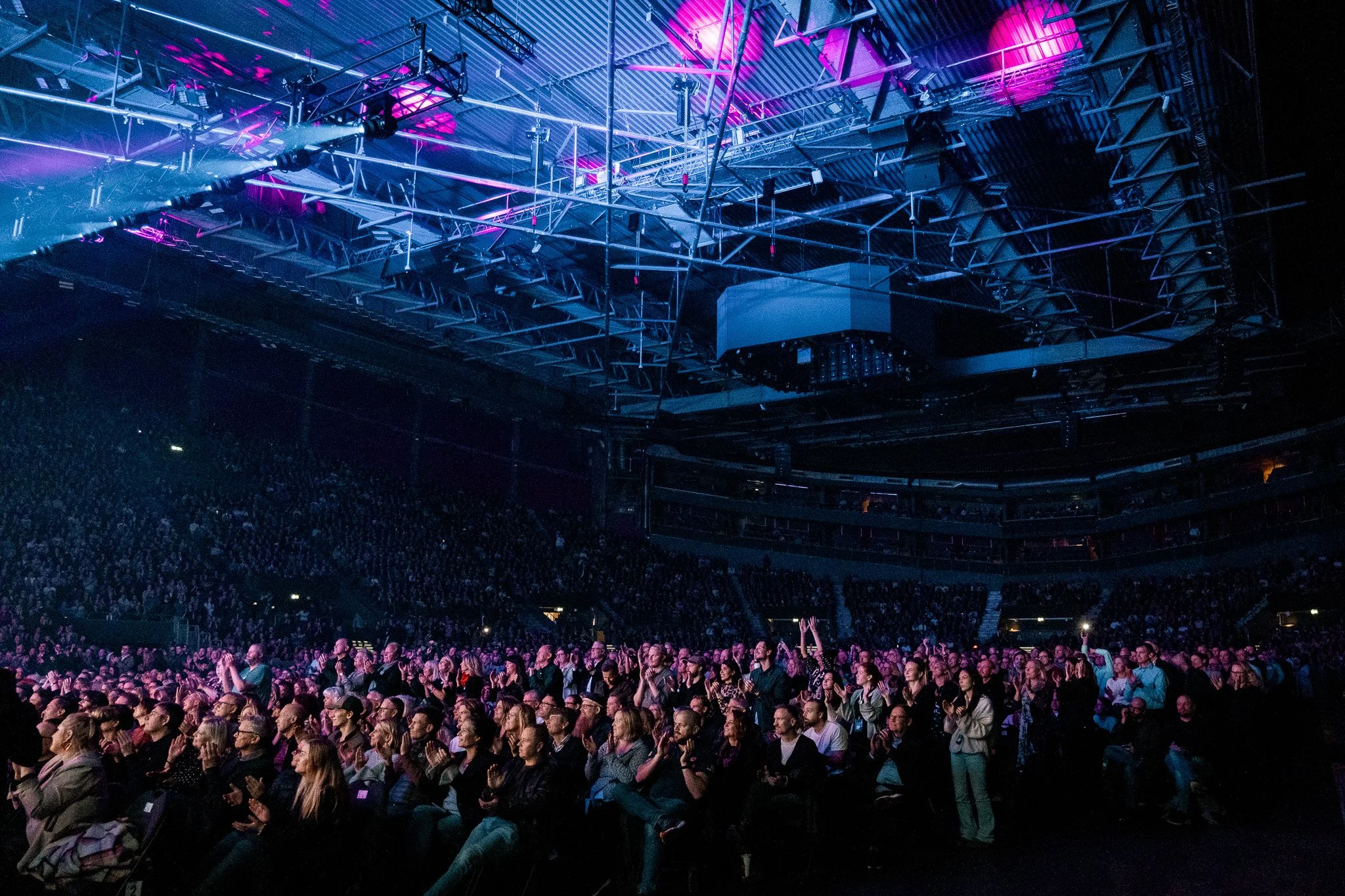 En stor publik i en arena under en konsert med färgglad belysning och ett komplext ljud- och ljussystem i taket.