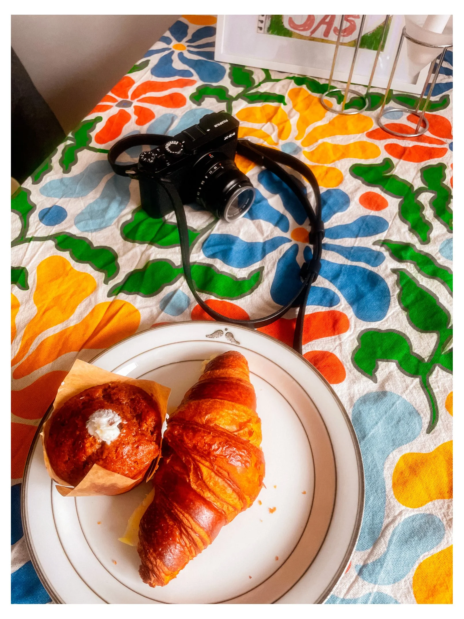En tallrik med två bakverk, en muffin och en croissant, på ett dekorativt bord med ett kamerasystem i bakgrunden.