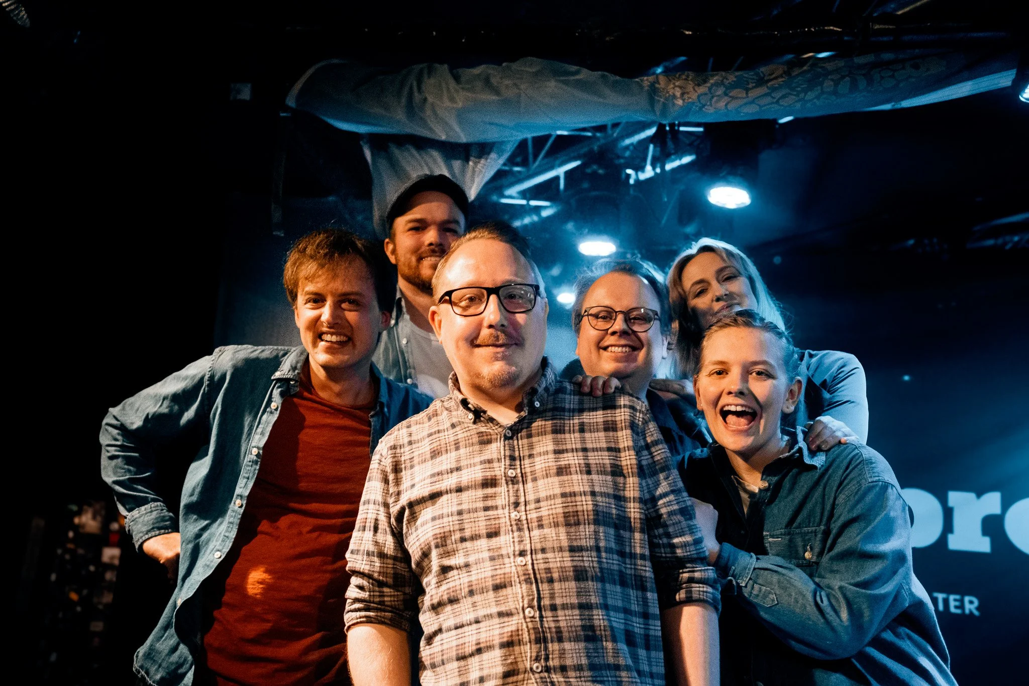 En grupp människor som ler och poserar framför en scen med blått ljus.