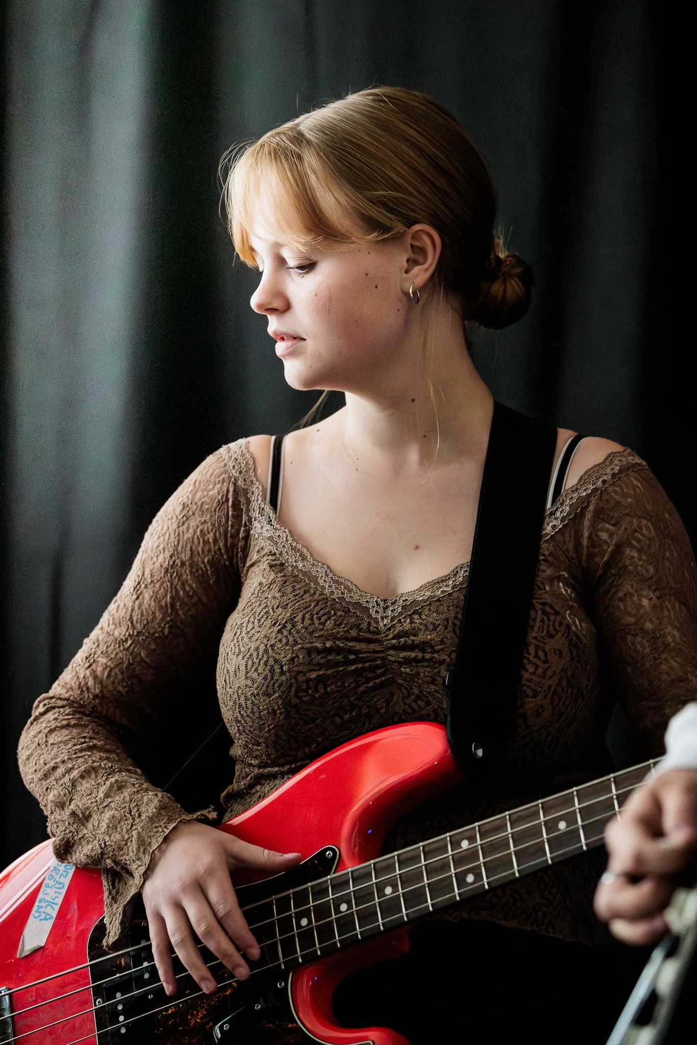 Kvinna med rött hår som spelar elbas, bär en brun spetsig tröja och har en svart axelrem.