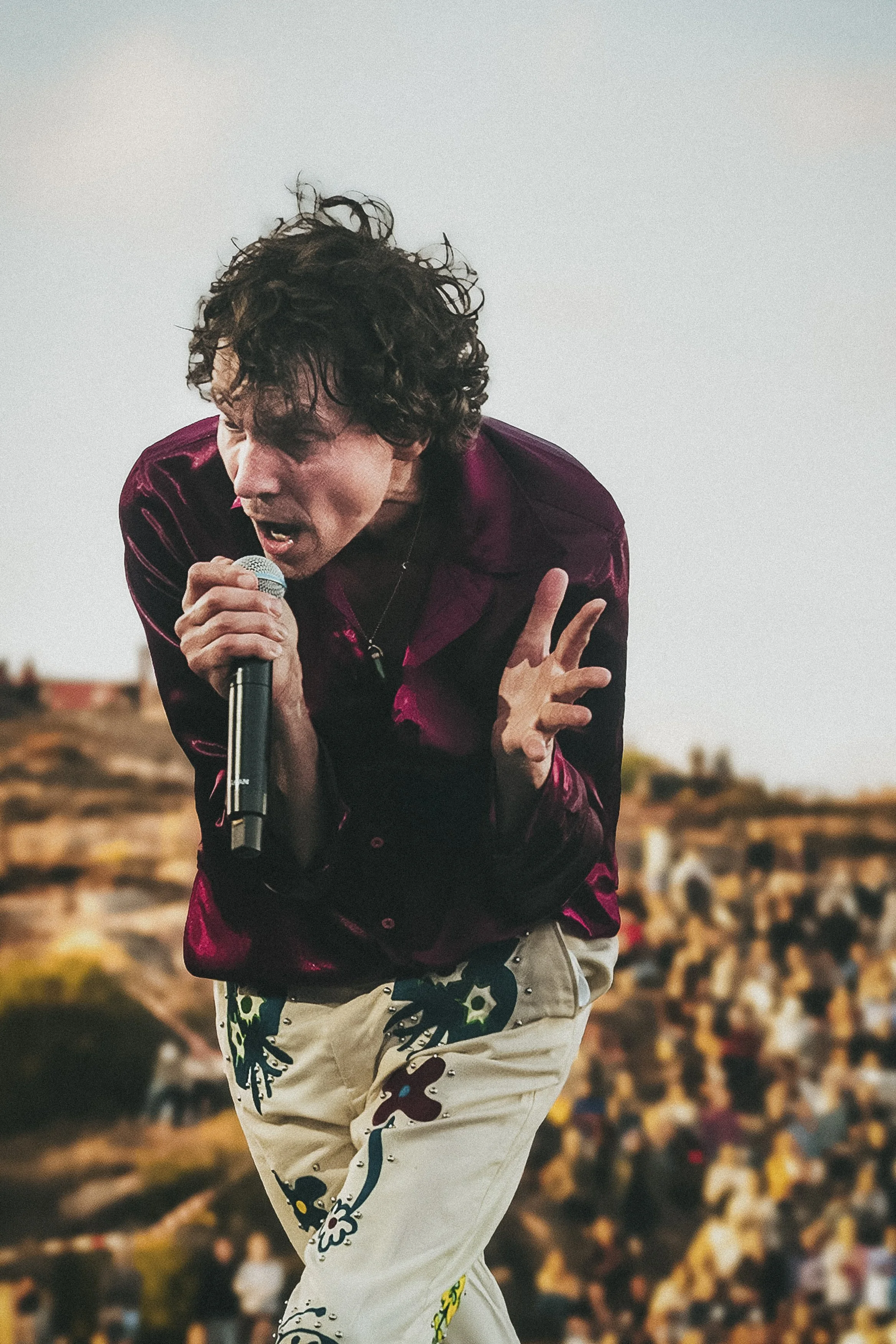 En man som sjunger eller talar i en mikrofon på scen med en publik i bakgrunden, utomhus.