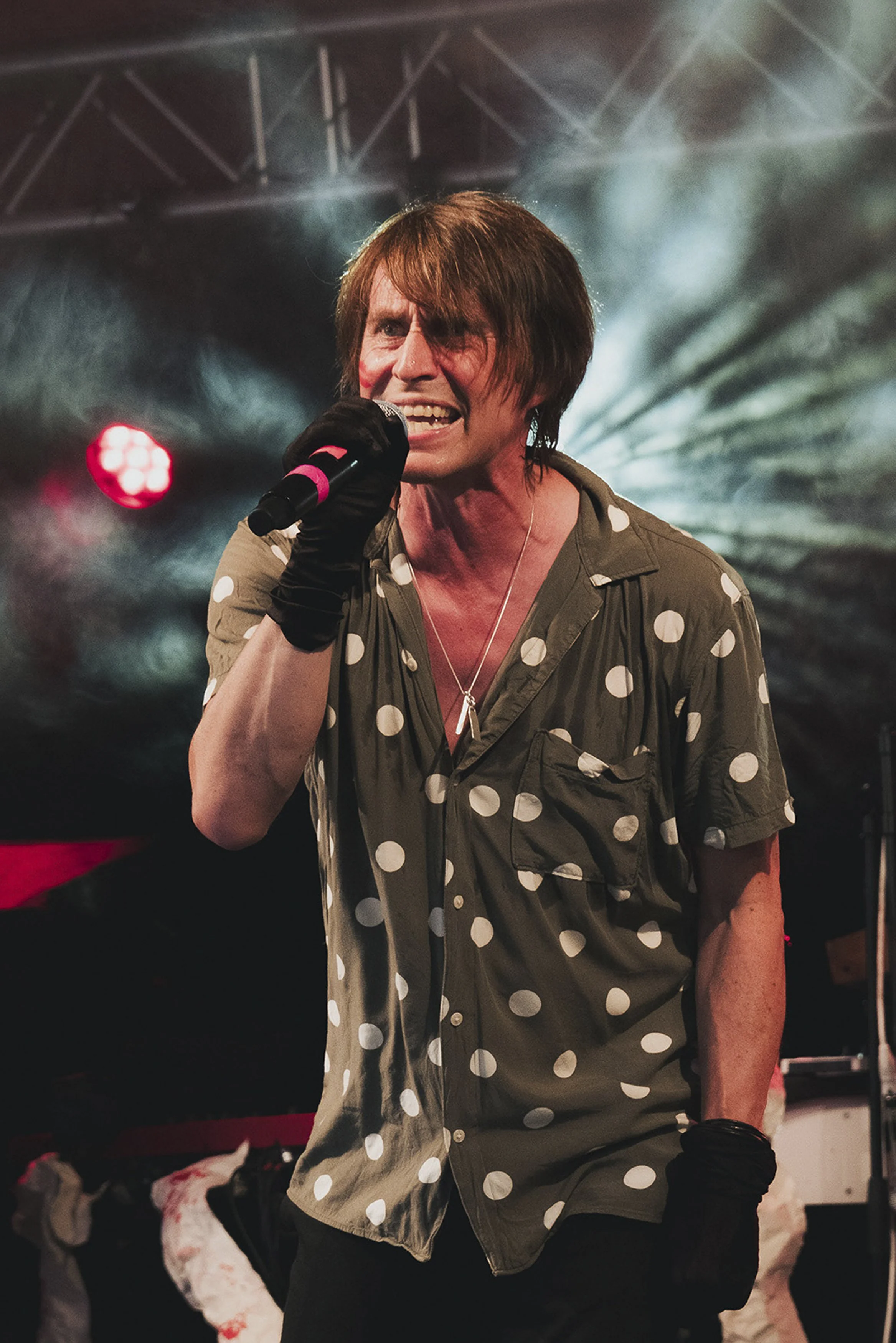 En man som sjunger på scenen, håller i en mikrofon, med stark scenbelysning i bakgrunden.