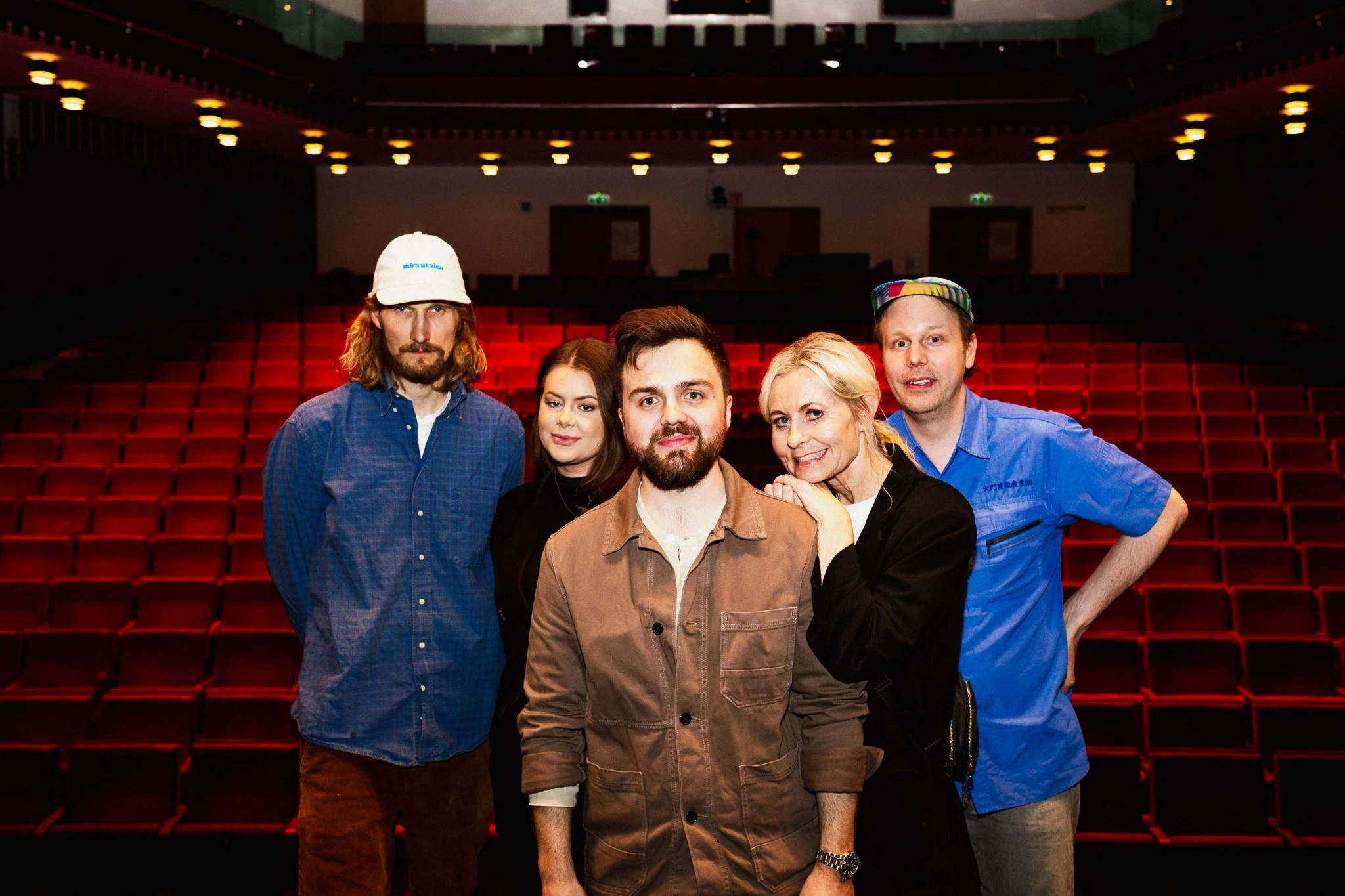 Fem personer står framför tomma röda biosalongsstolar i en mörk salong, de tittar mot kameran och ler.