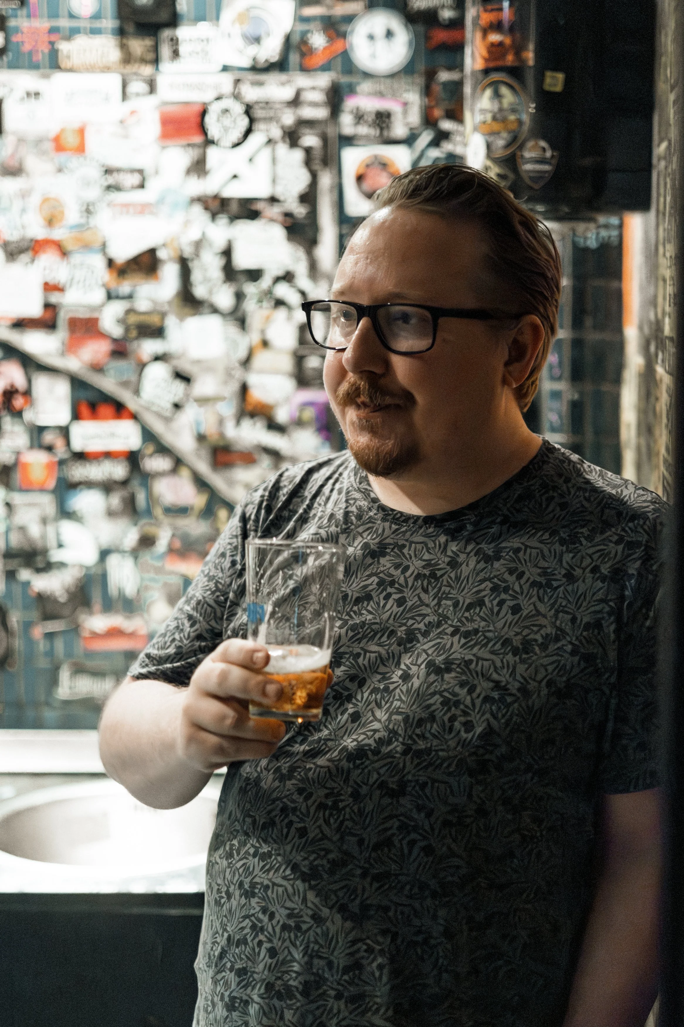 Man som dricker ett glas öl i en bar med väggdekoration av stickers och memorabilia.