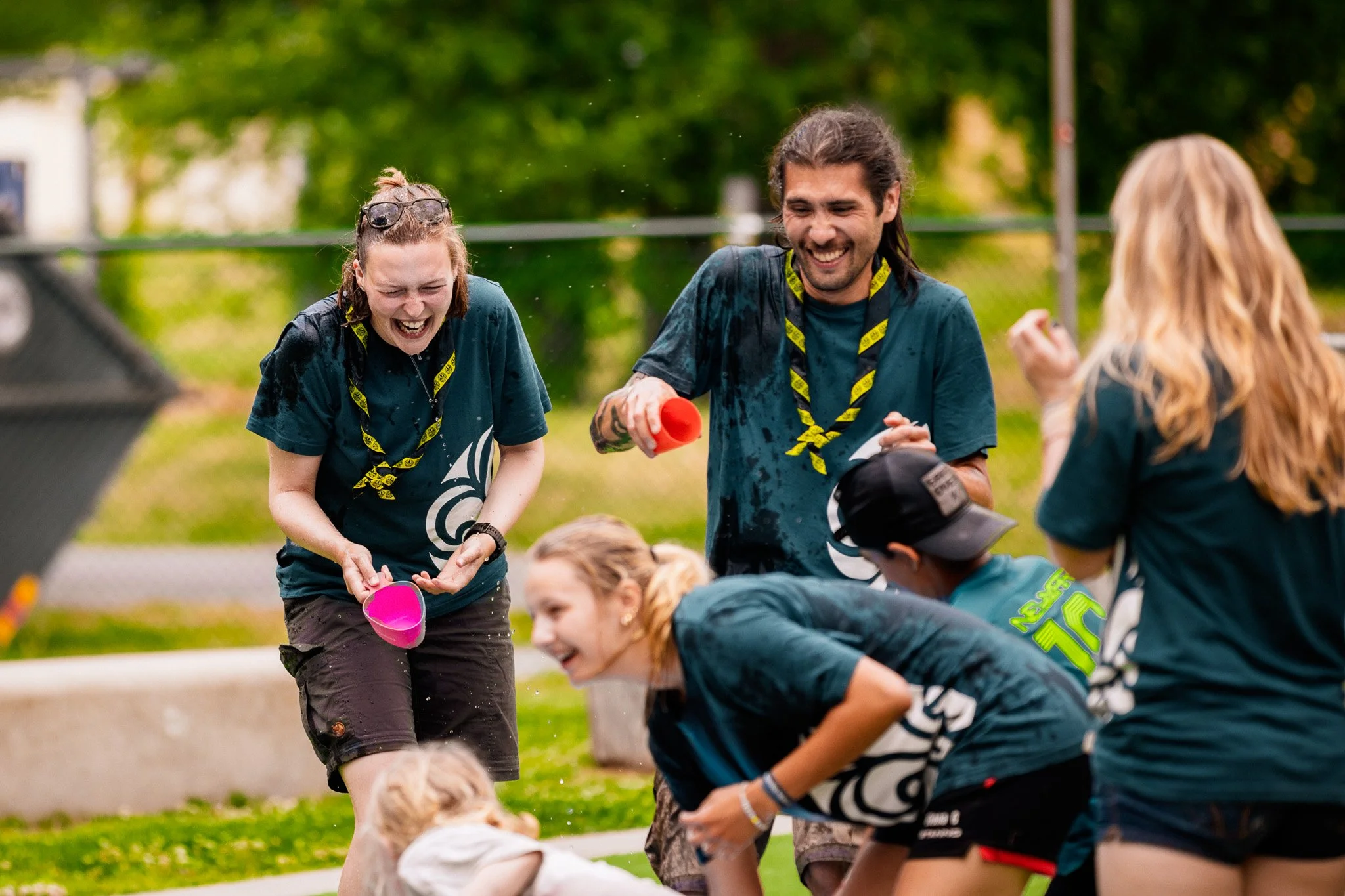 Grupp människor leker vattenlekar utomhus, alla är våta och skrattar.