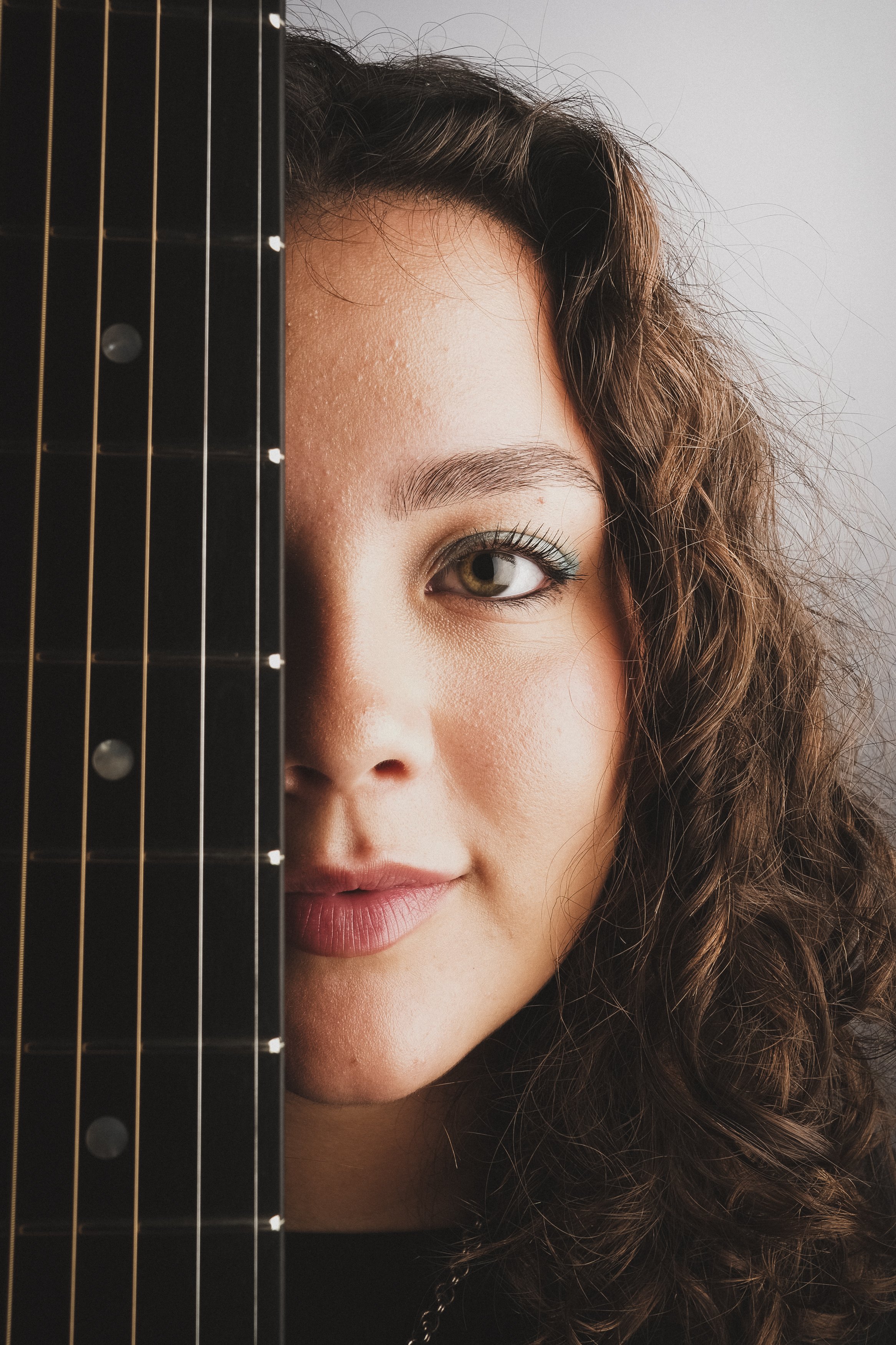 Närbild av en ung kvinna med lockigt hår som tittar bakom en gitarr.