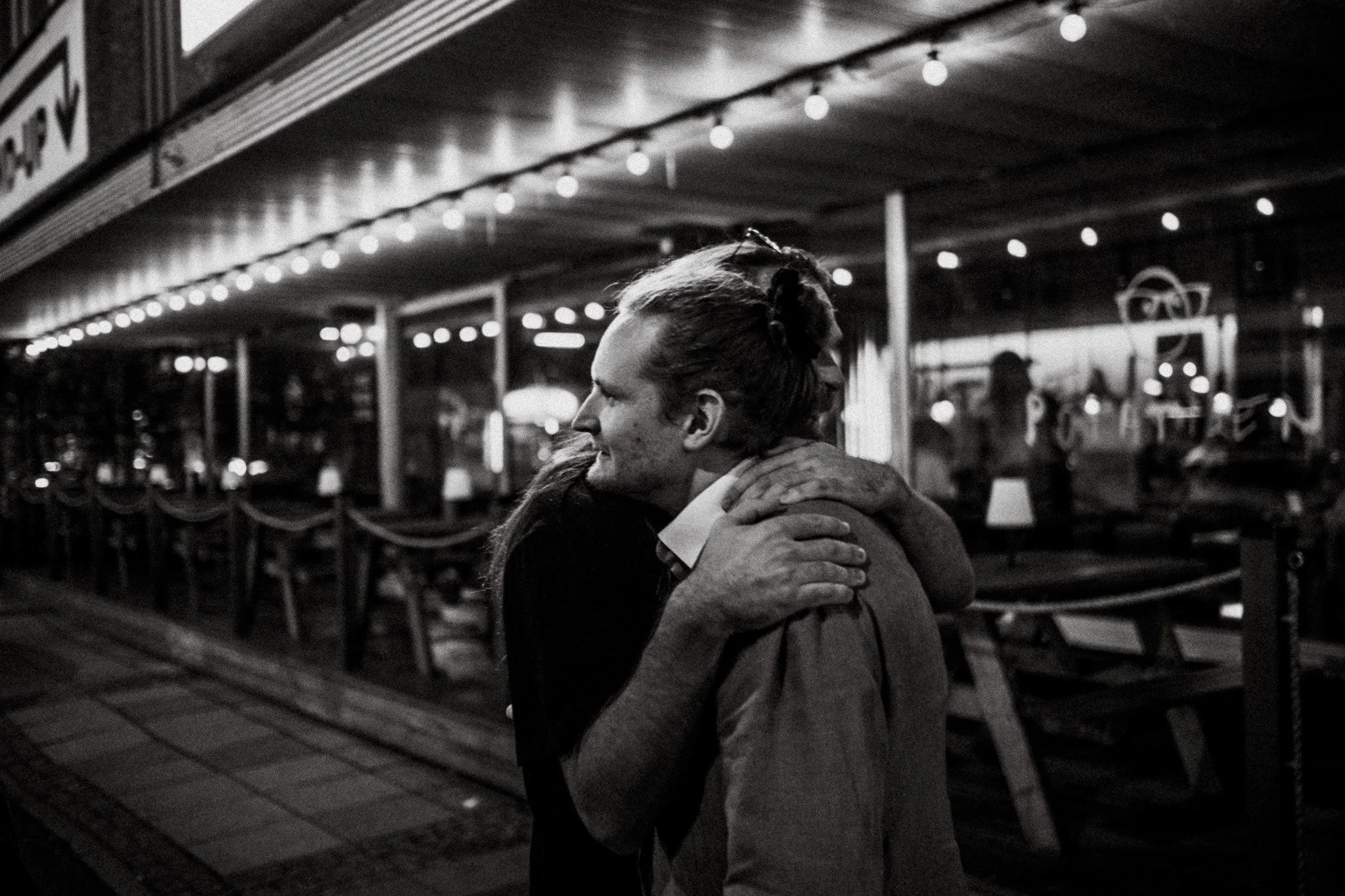 Två personer som kramas utanför en restaurang på kvällen, svarta och vita fotografi.