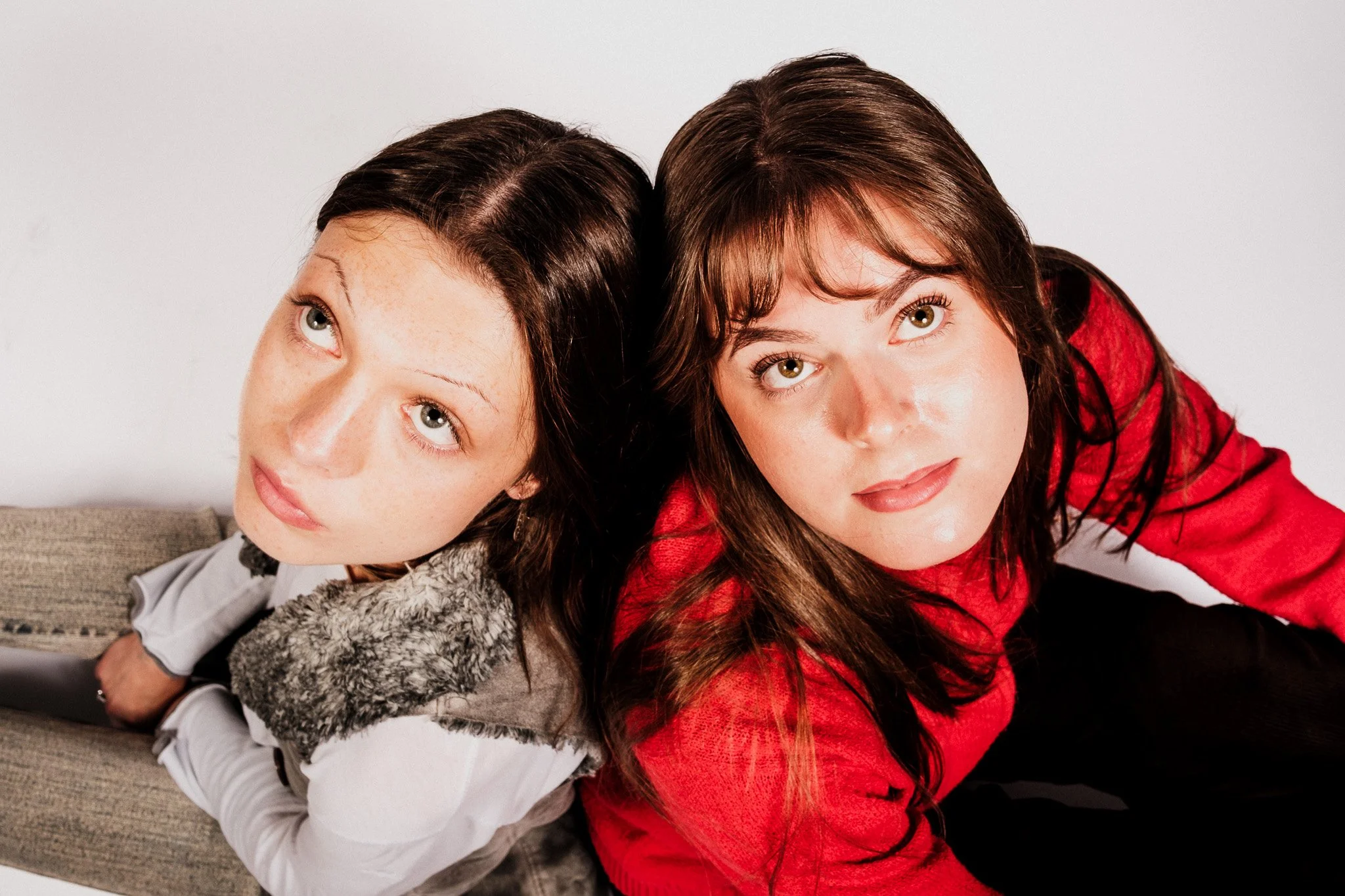 Två unga kvinnor ligger på en soffa, nära varandra, och tittar upp mot kameran.