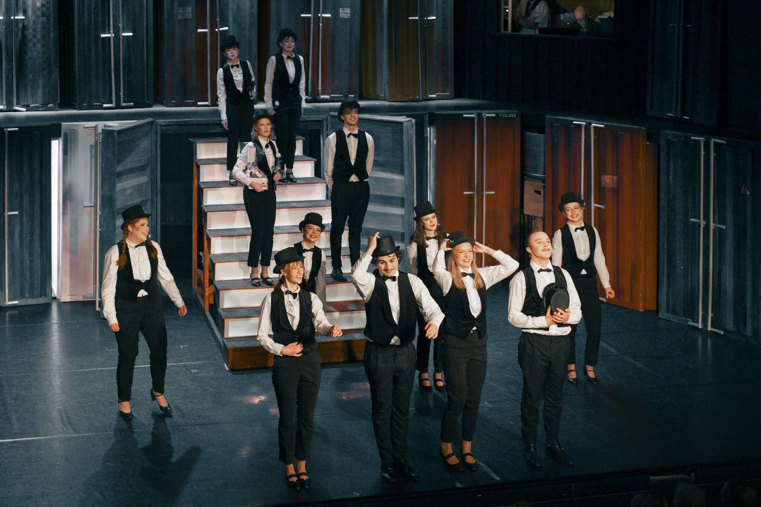 Ungdomar i svartvit kostym och hattar på scen, delta i teaterföreställning