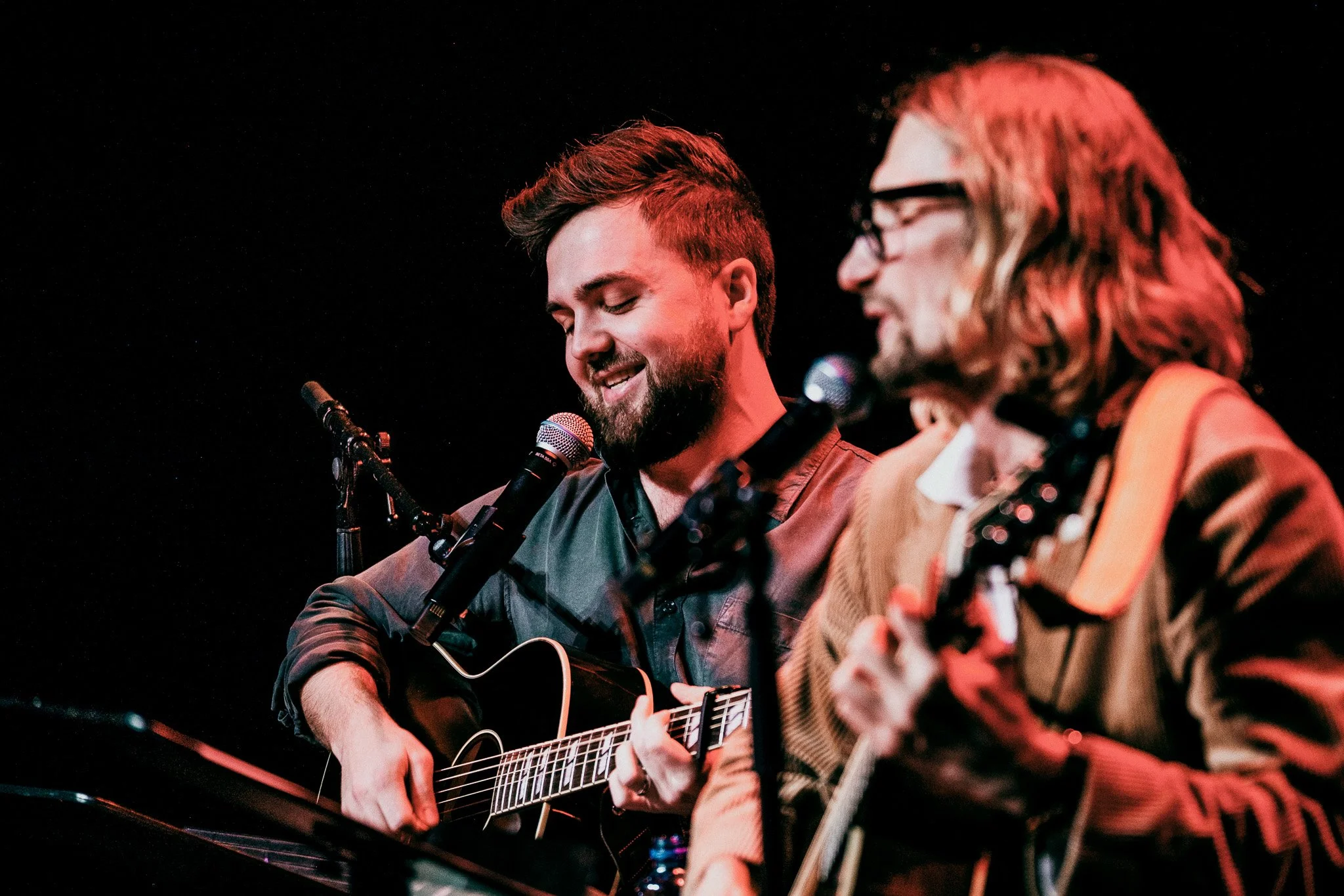 Två män som sjunger och spelar gitarr på scen, med mikrofoner framför.
