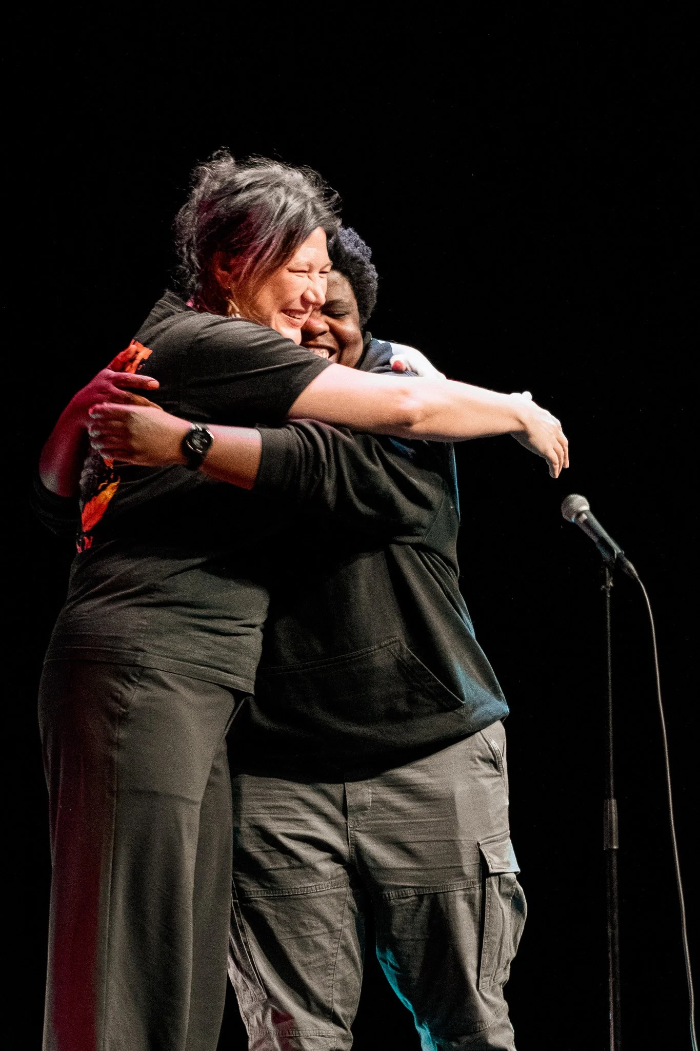 Två personer som kramas och skrattar på en scen med en mikrofon.