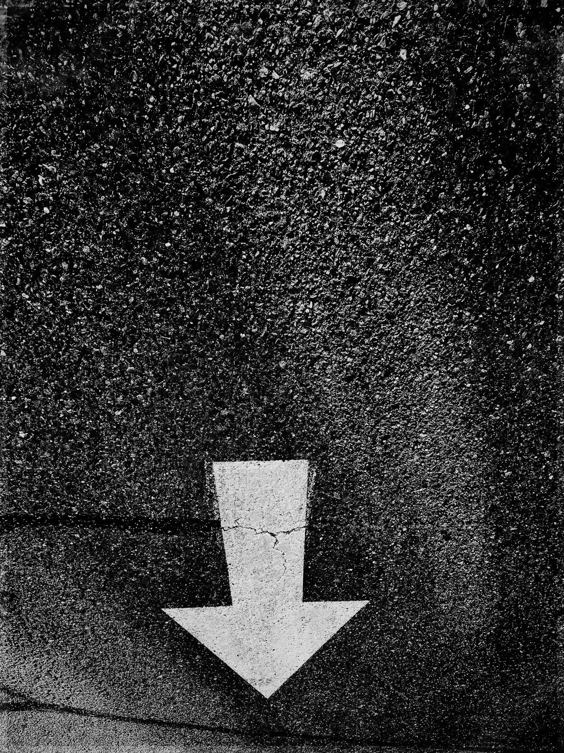 A white downward arrow painted on a dark textured asphalt surface.