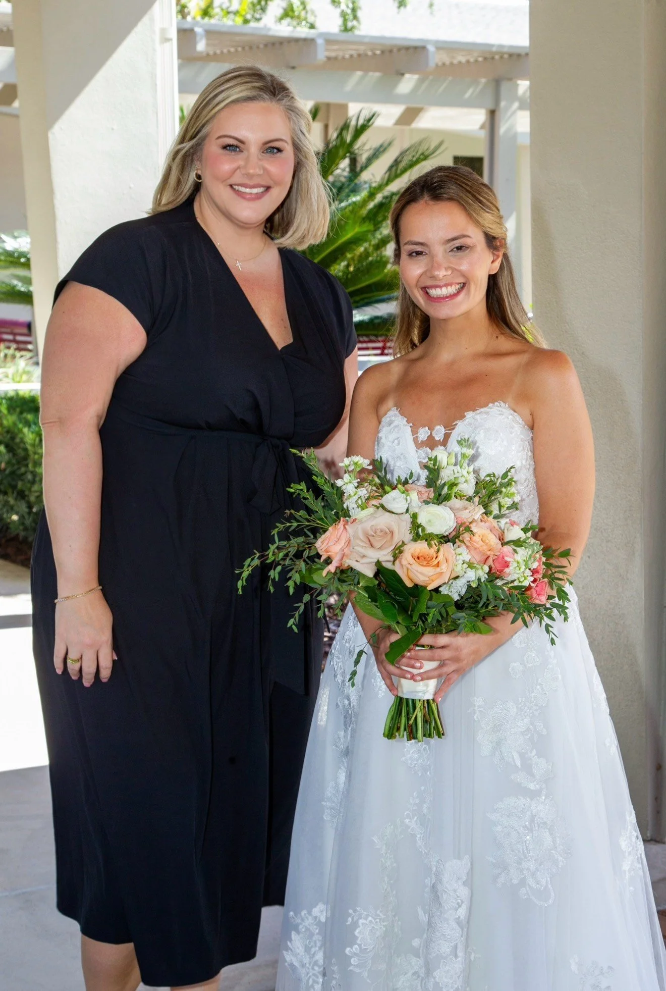 Bride Kimberly smiling beside her wedding planner from Something Blue Events while holding her peach, blush, and ivory bridal bouquet.