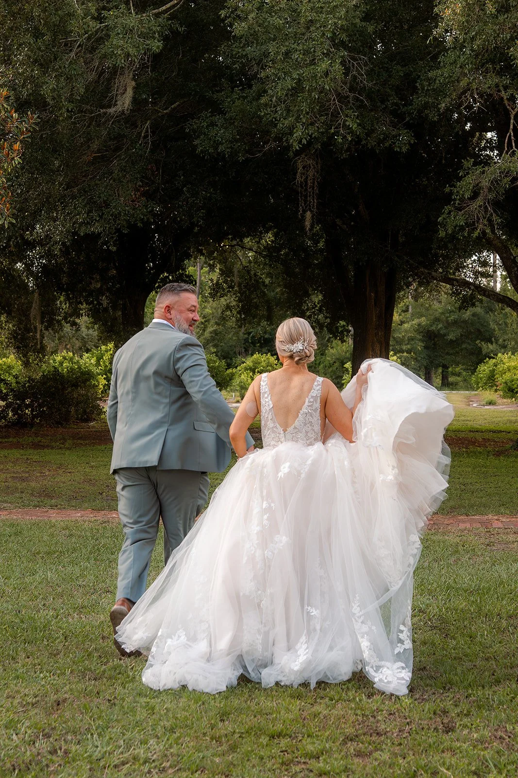 Tiffany shows the lace and tulle train of her ivory wedding gown while walking hand in hand with Matthew after their Florida wedding.