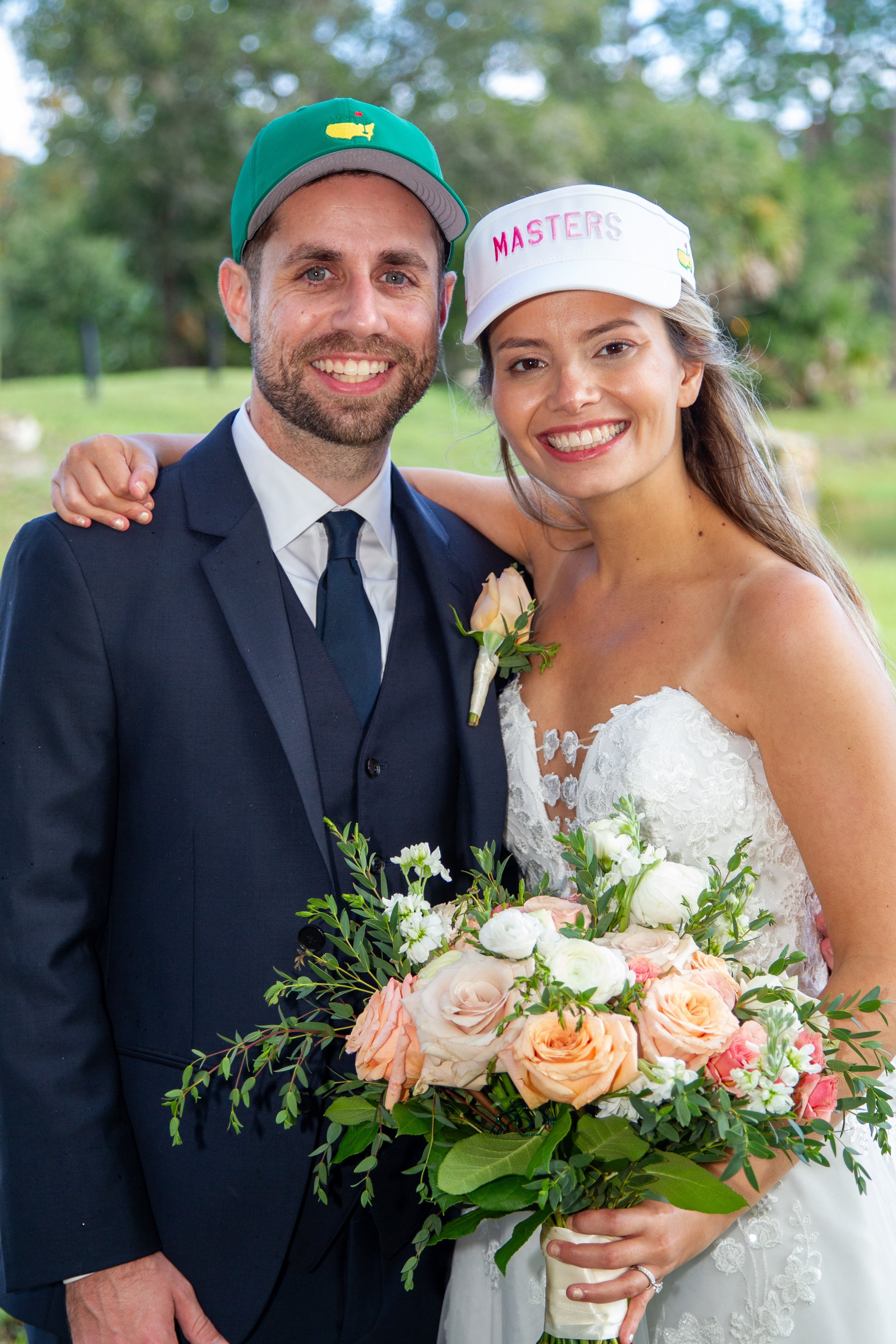 Newlyweds Kimberly and John smiling in Masters golf hats, with Kimmy holding a peach and ivory bridal bouquet at Heathrow Country Club.