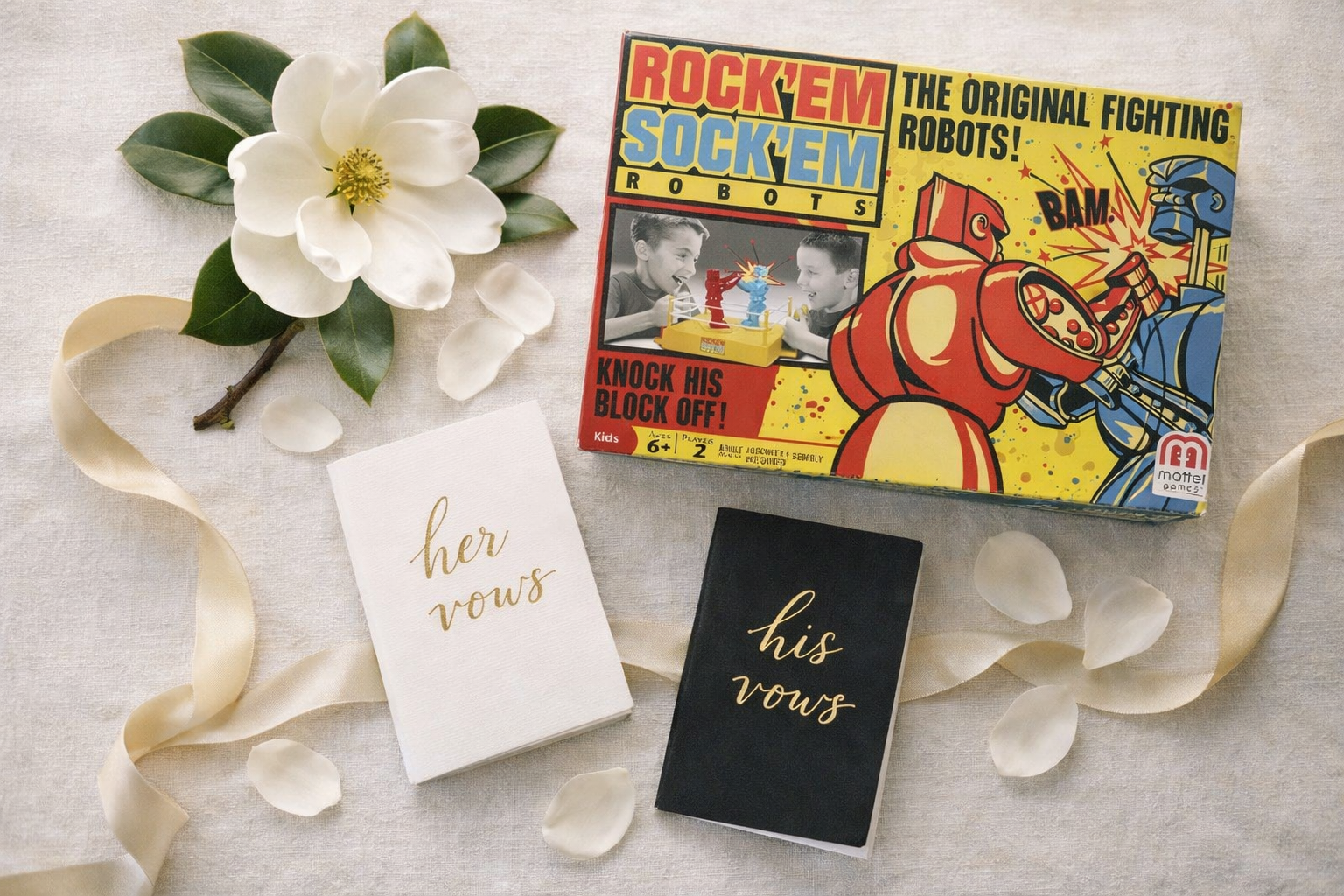 A flat lay of vow books, a magnolia and Rock 'em, Sock' em robots.