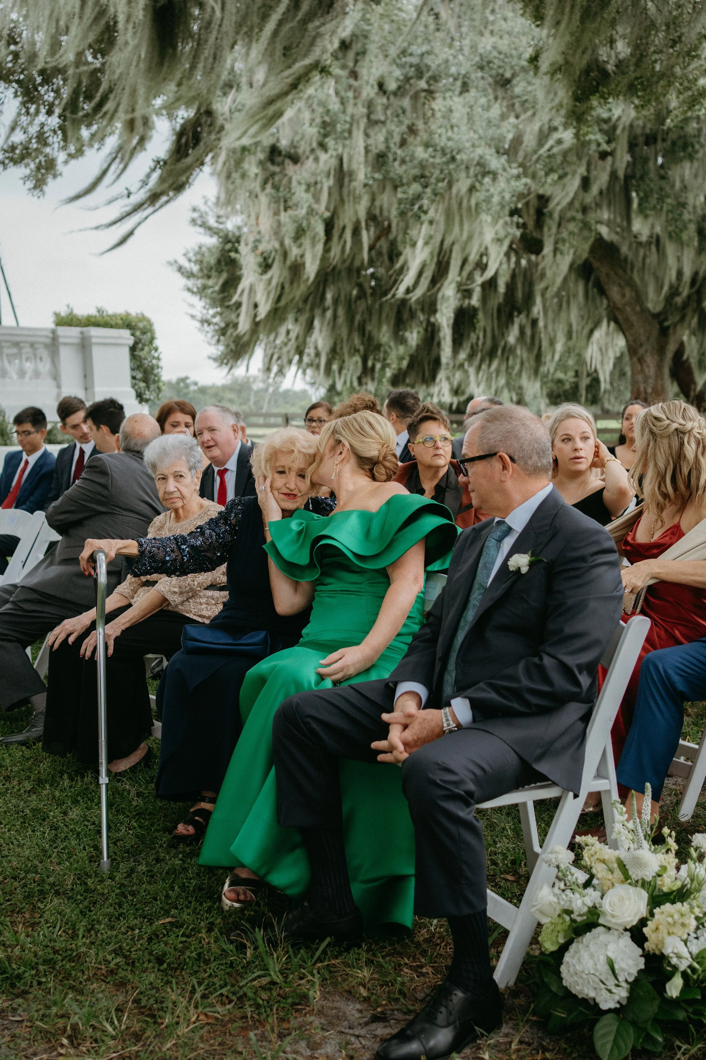 Wedding guests sharing a tender family moment beneath the oak tree at Bella Cosa before the outdoor ceremony.