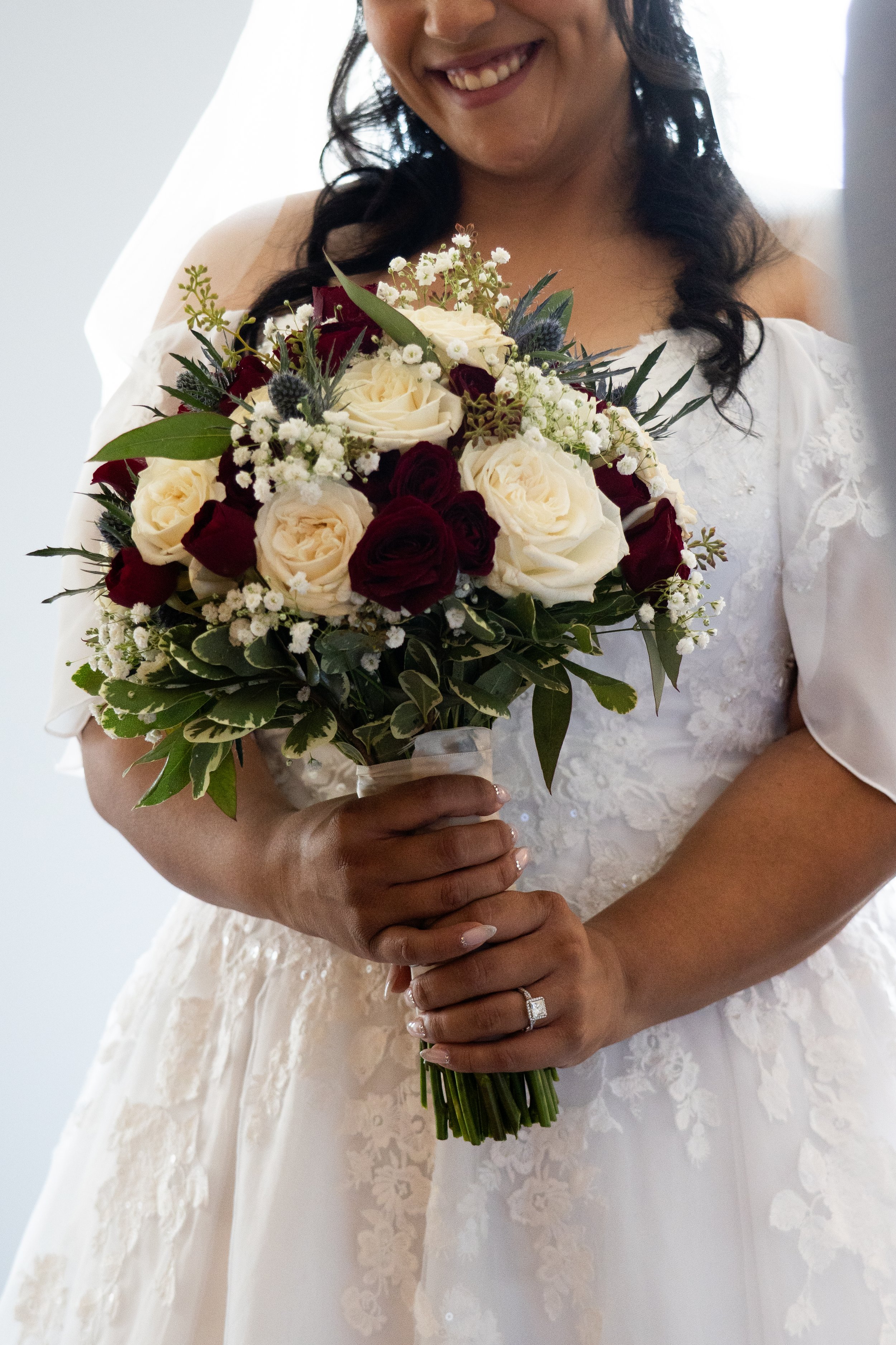 A beautiful bride to be in a white wedding dress holding a bouquet of white and red roses with greenery.