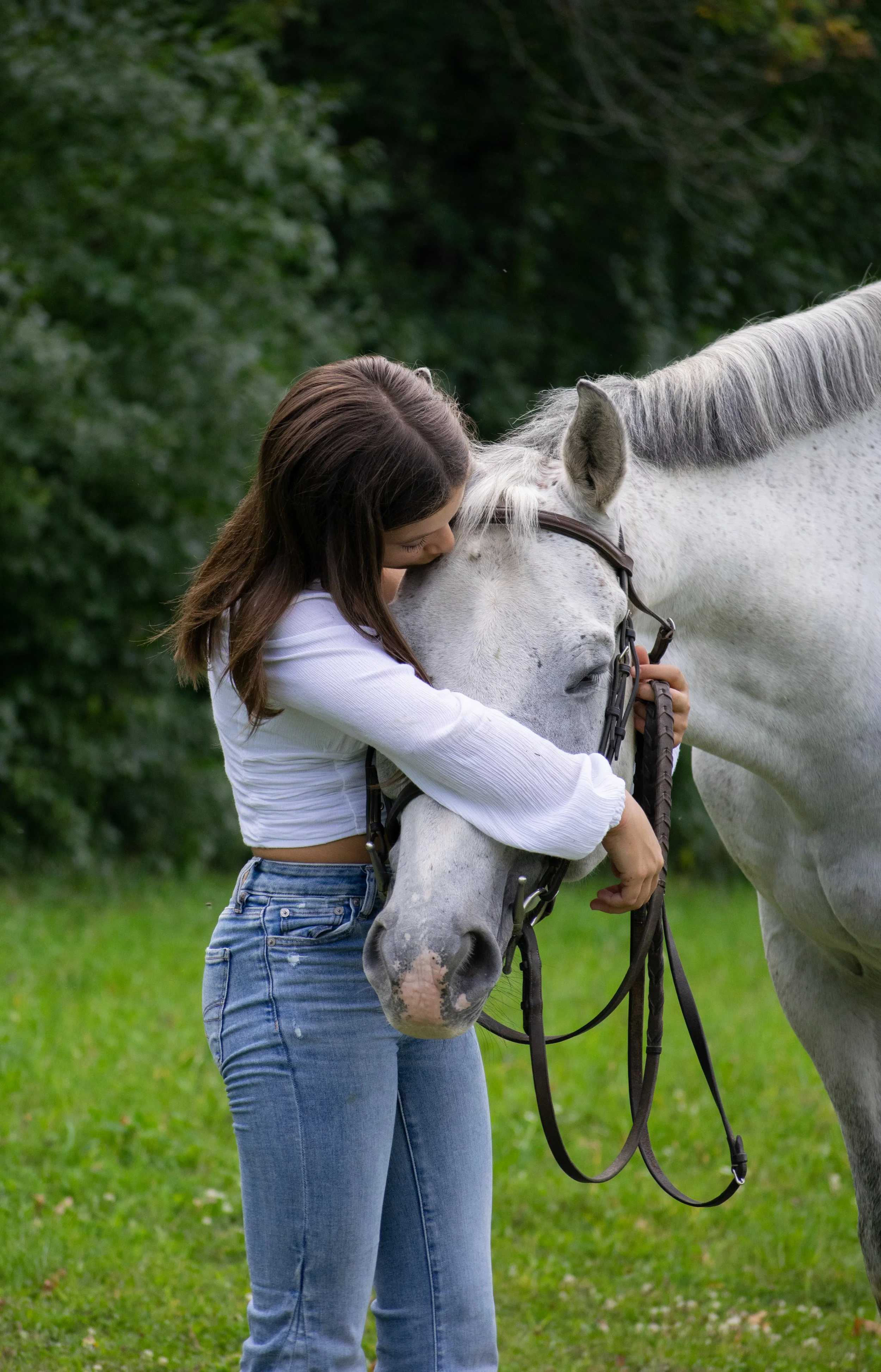 A young woman hugging a white horse outdoors on a grassy field.