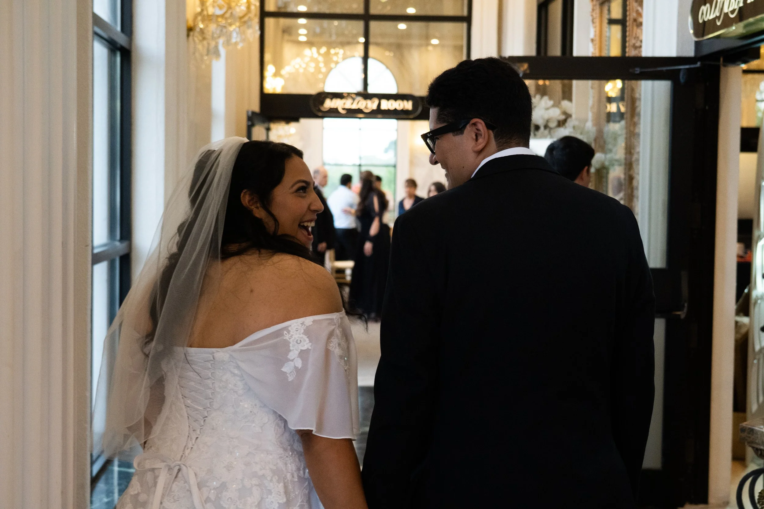 A bride and groom smiling and looking at each other inside a decorated venue during their wedding celebration.