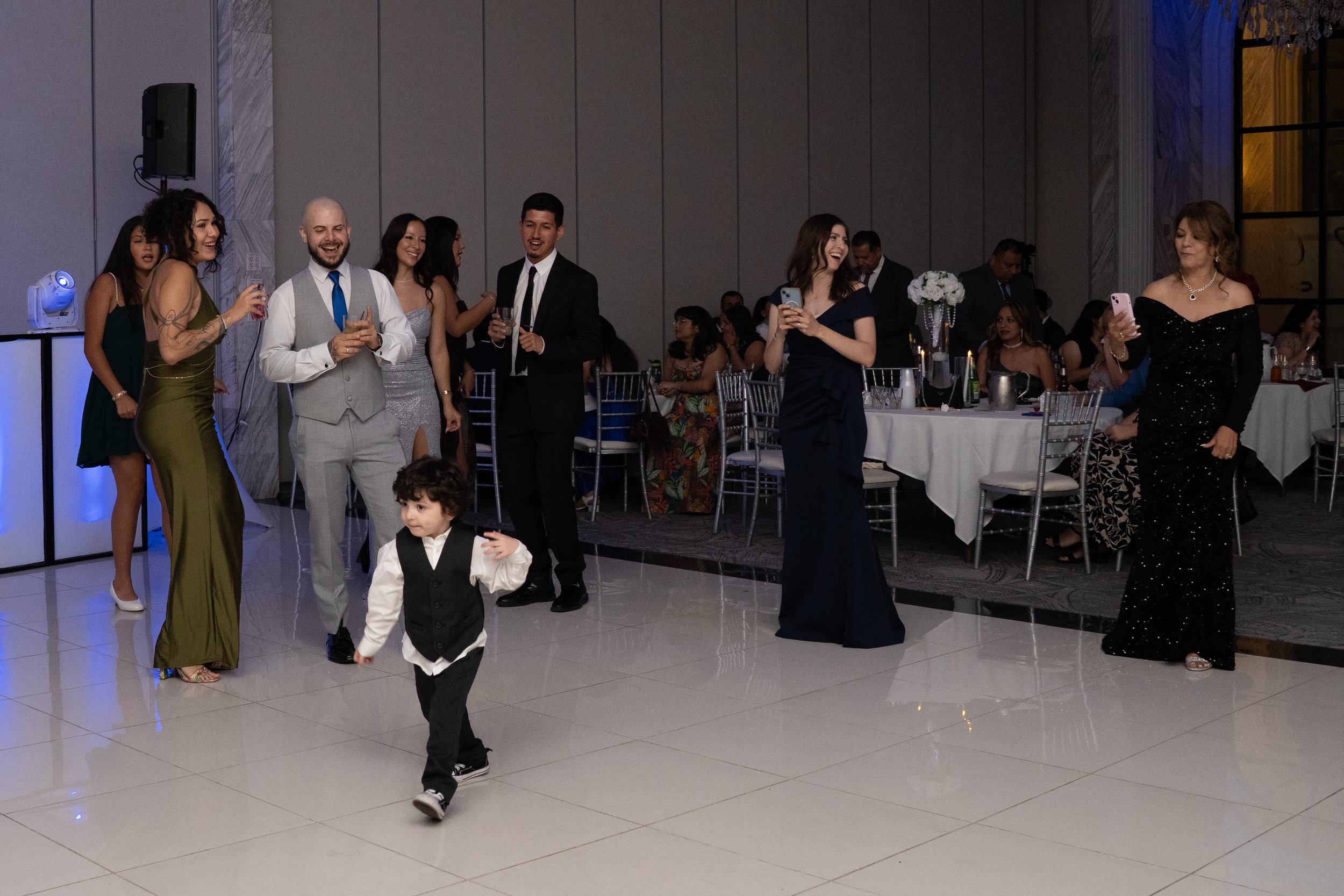People dancing and socializing at a formal event or wedding reception in a banquet hall, with a child walking in the foreground.