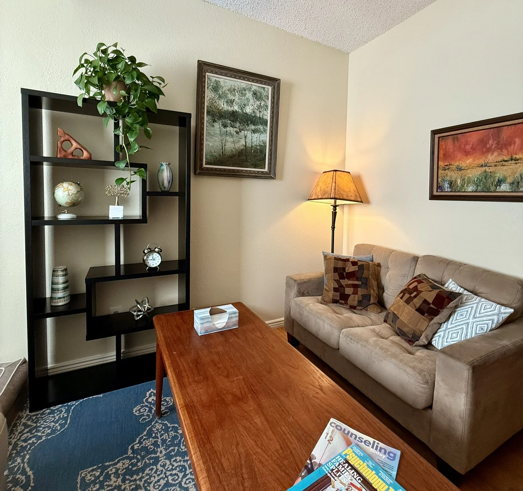 Interior scene with two mustard-colored armchairs facing each other, a potted Monstera plant between them, white curtains in the background, and two tall floor lamps flanking the setup. One armchair has a color calibration chart, and the other has a clapperboard with production notes.