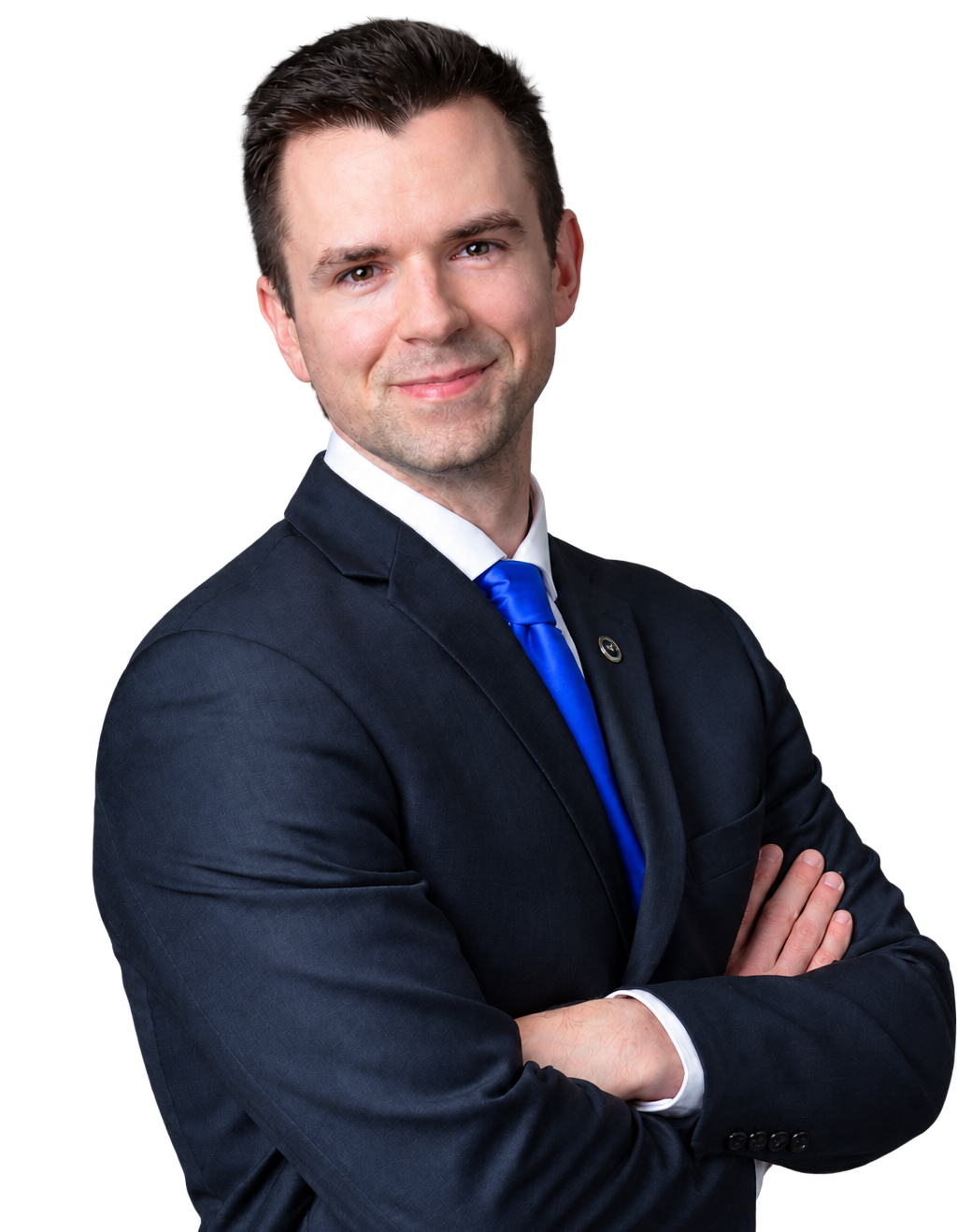 A young man in a dark suit with a white shirt and blue tie, standing with arms crossed and smiling at the camera.