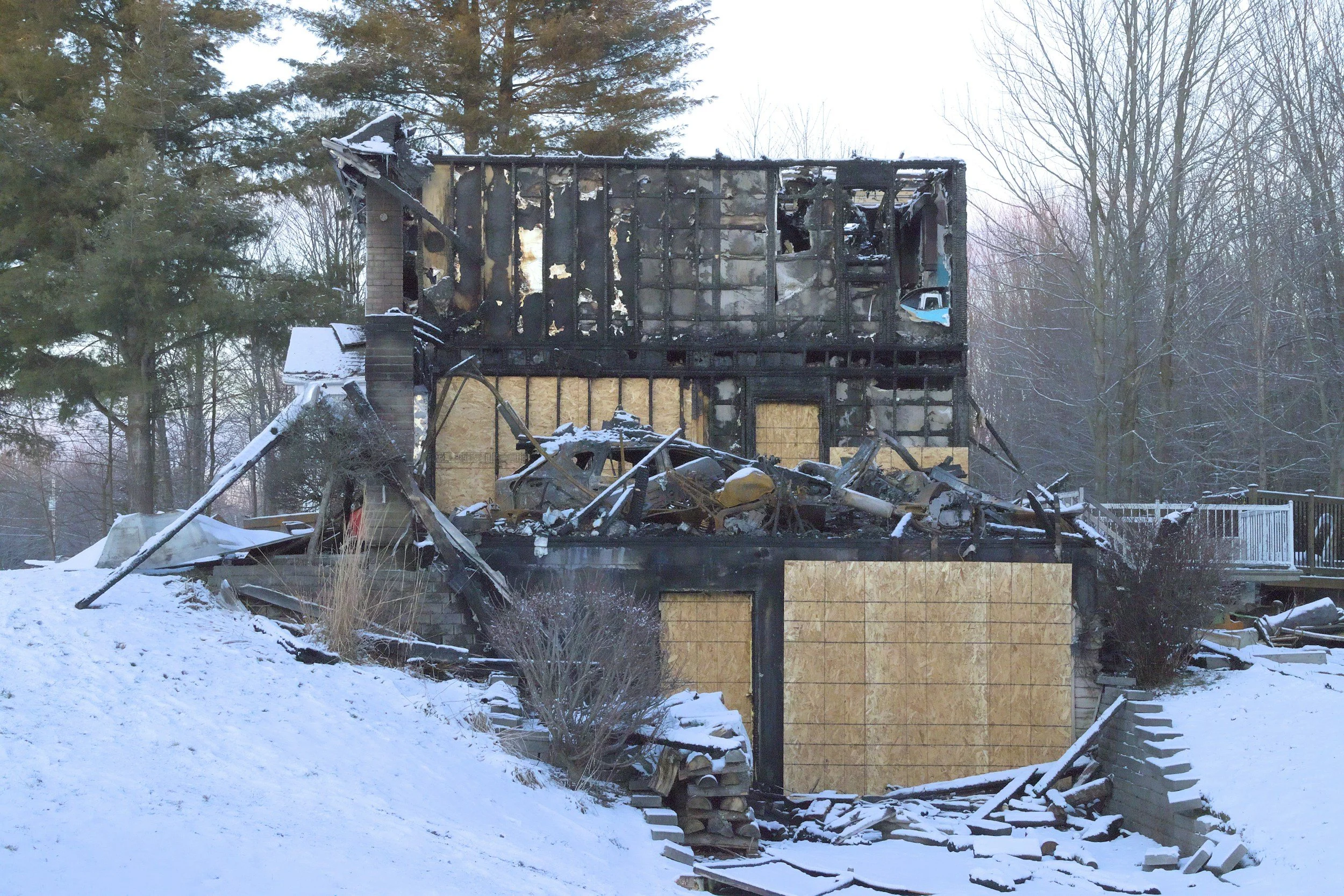A house severely damaged by fire, with the roof and walls burned, debris in front, and snow on the ground in St Louis County
