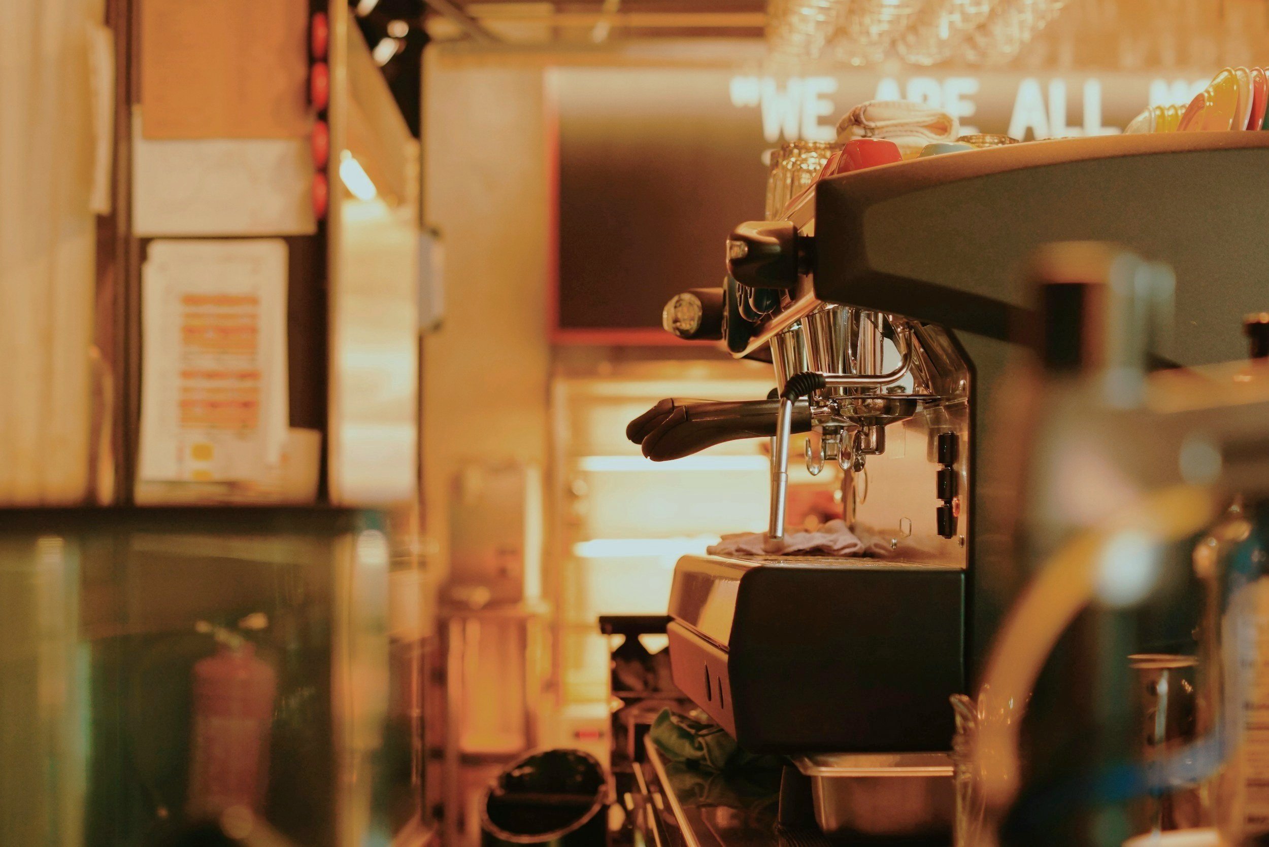 Close-up of a commercial espresso machine on a counter in a cafe, with a warm glow in the background.