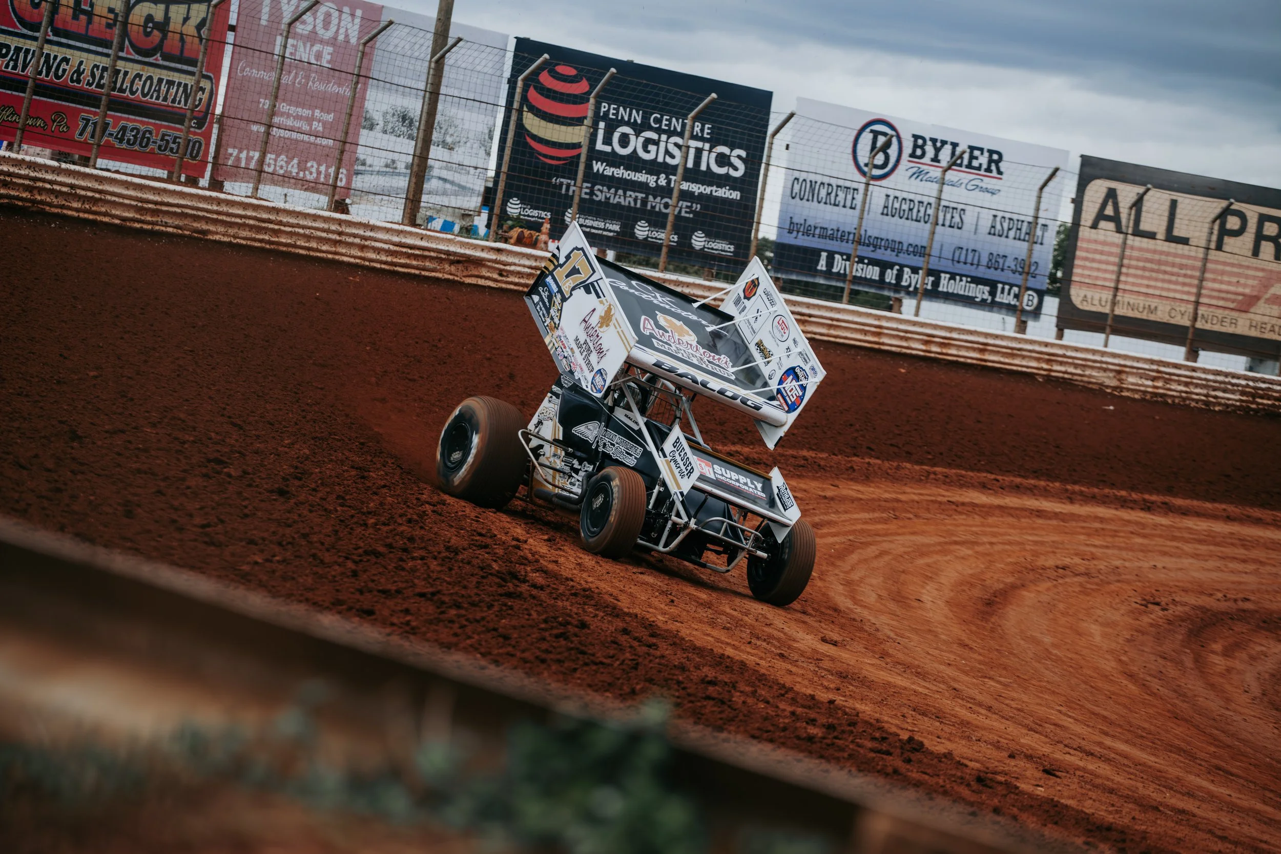 A sprint car racing on a dirt track with a blurred background and a large black wing with white and red lettering.