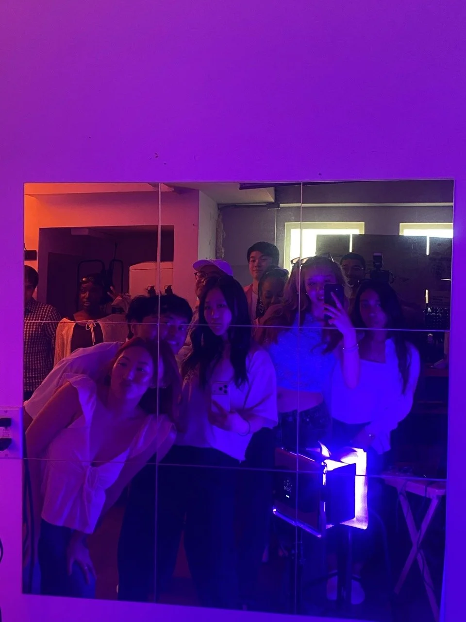 Group of friends taking a mirror selfie in a dimly lit room with purple and neon lighting.