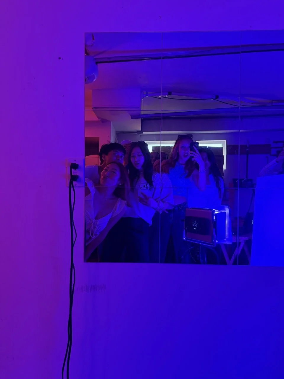Group of five young women taking a mirror selfie in a dimly lit room illuminated by purple and blue lights.