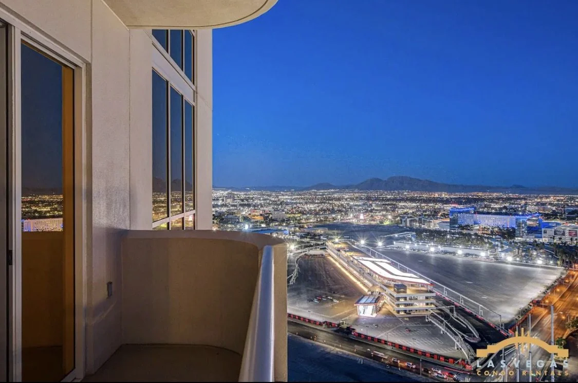 Night view of Las Vegas from the balcony showing the cityscape, the Formula 1 Grand Prix race paddock,  and mountains in the distance.