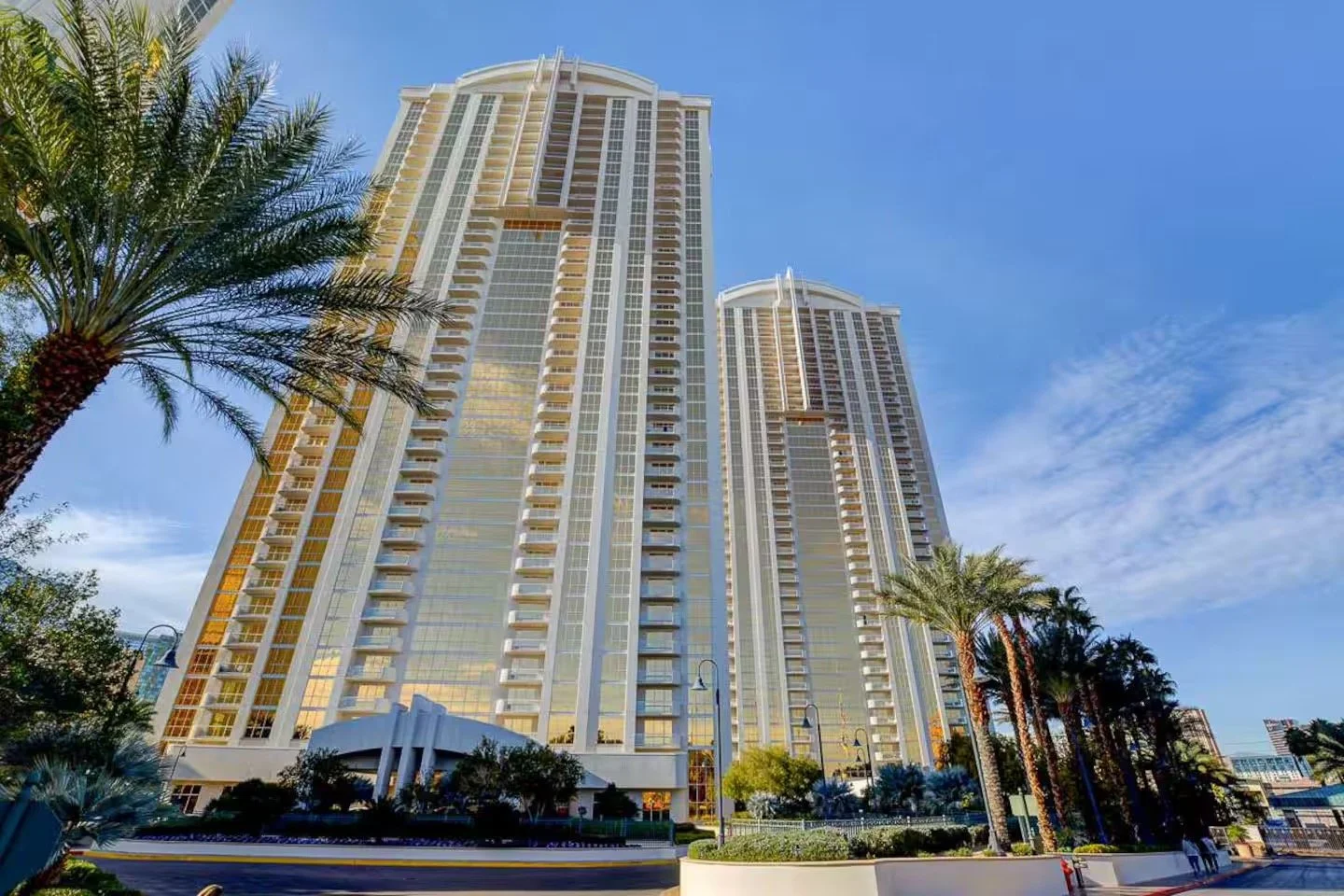 Tall MGM Signature Las Vegas skyscraper with glass exterior reflections, surrounded by palm trees and a clear blue sky.
