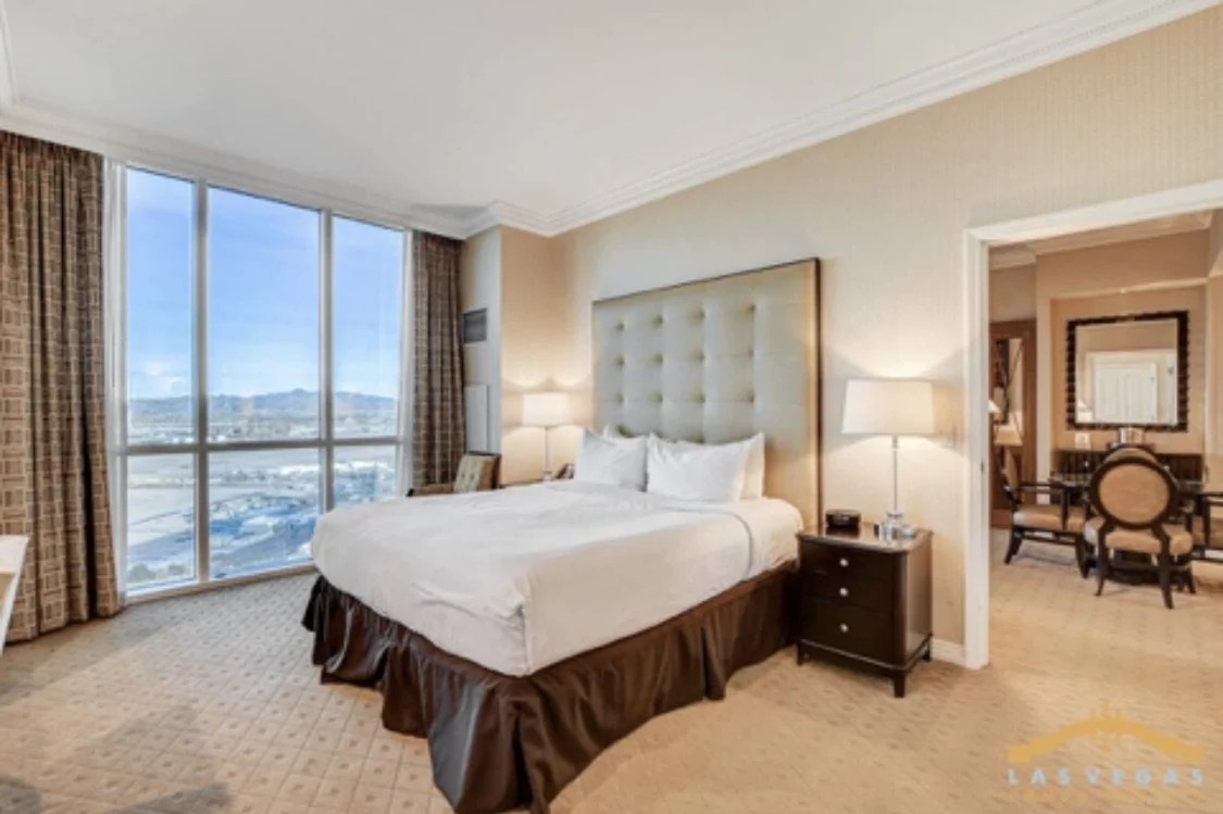The penthouse  bedroom with a large king bed, nightstands with lamps, and floor to ceiling windows with a city view.