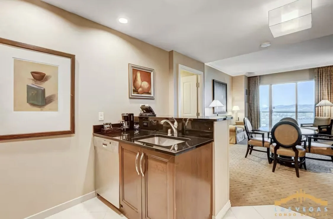 Interior view of the condo suite with a kitchen and a living room with large window showing cityscape and mountains in the background.