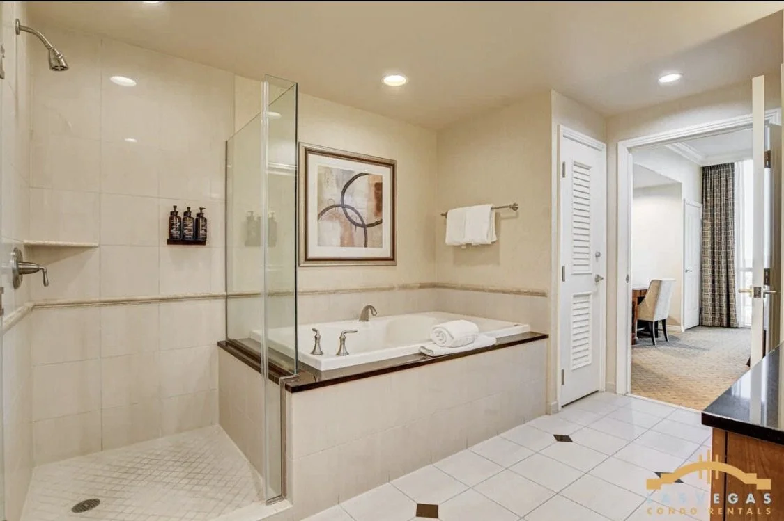 Master bathroom with a walk-in shower, jetted bathtub, and an open door leading the bedroom sitting area desk and chair.