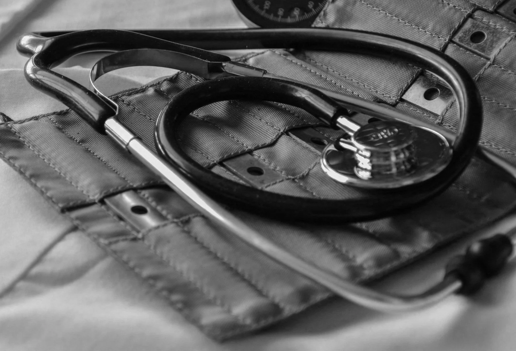 Close-up of a stethoscope resting on a medical pouch, in black and white.