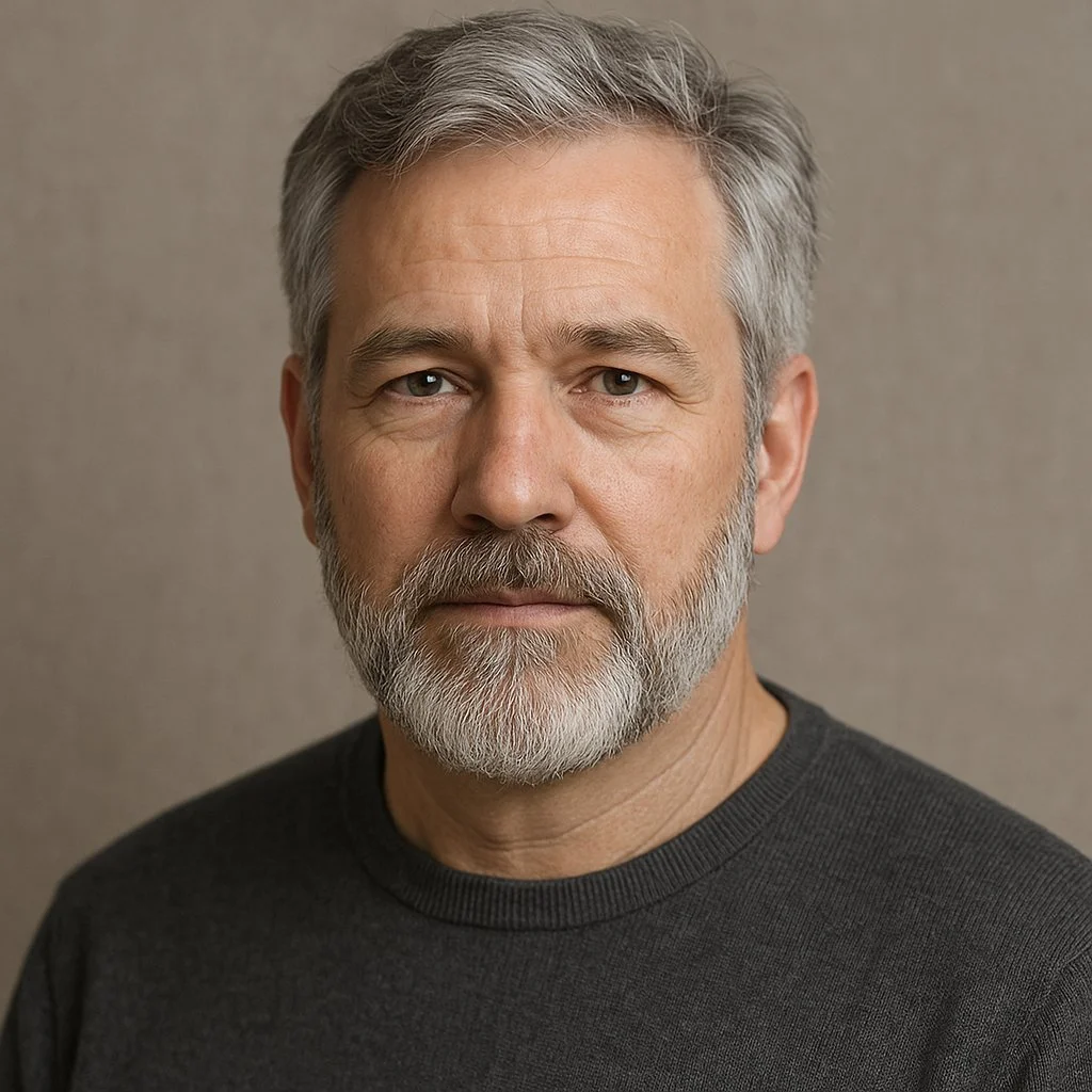 A close-up portrait of a middle-aged man with gray hair and a beard, wearing a dark sweater, looking directly at the camera with a neutral expression.