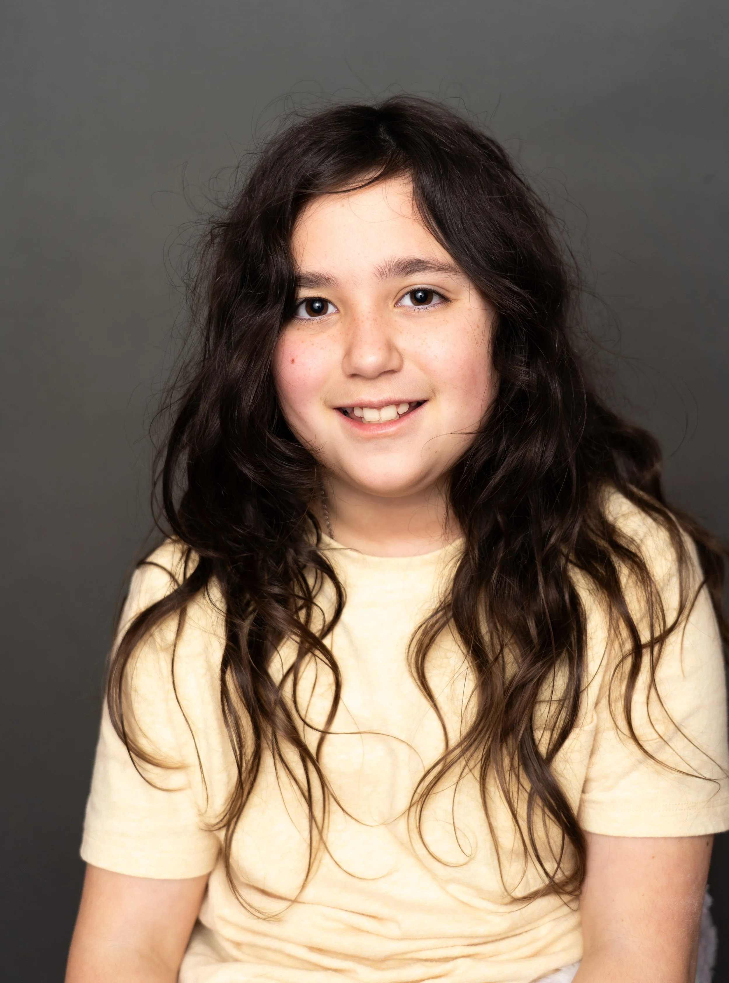 Natural school portrait of a smiling girl photographed on a gray studio background.
