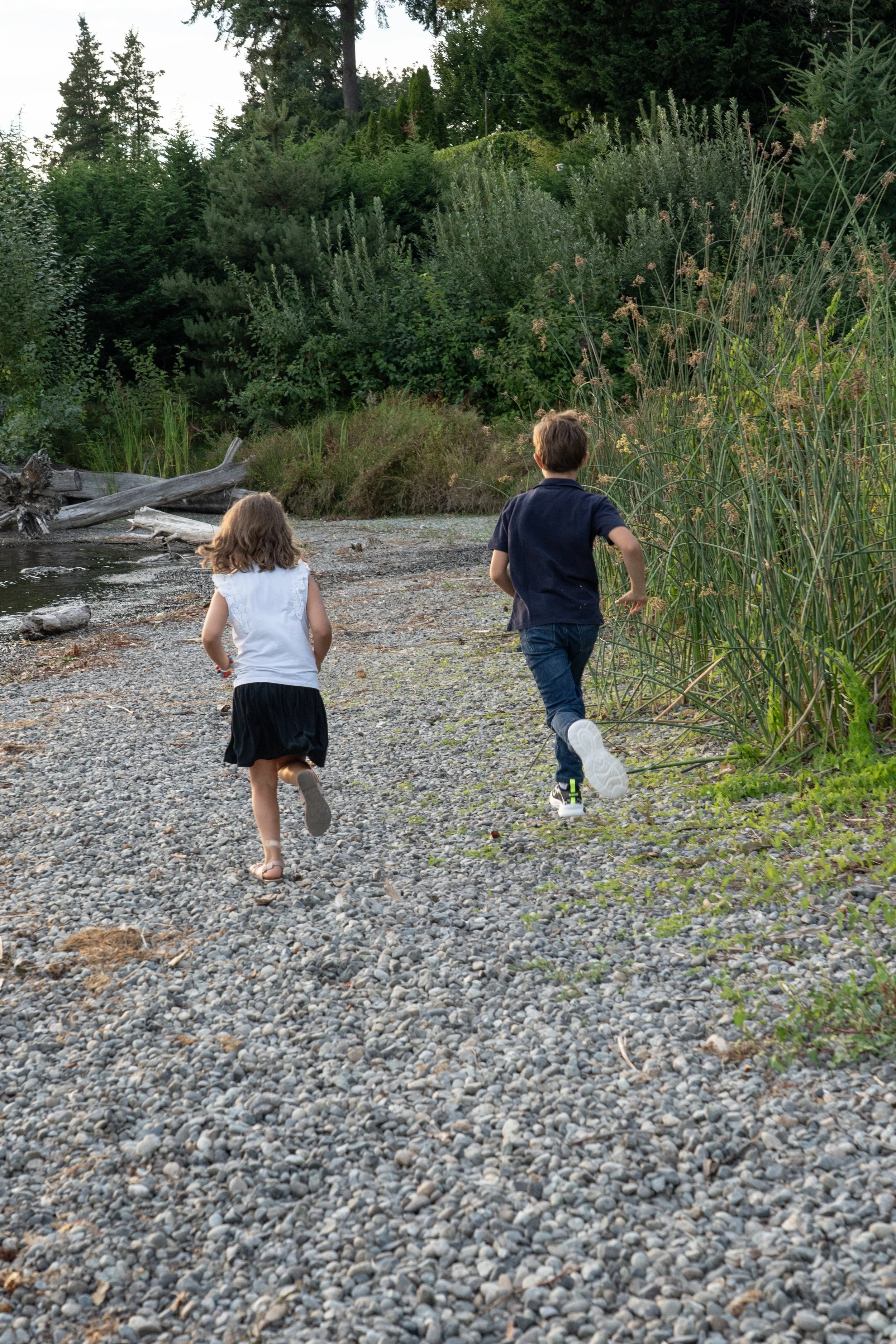 Two siblings run along the shoreline during a sunset family photography session on Mercer Island. Documentary-style family photography captures genuine moments of play, adventure, and connection instead of stiff poses.
