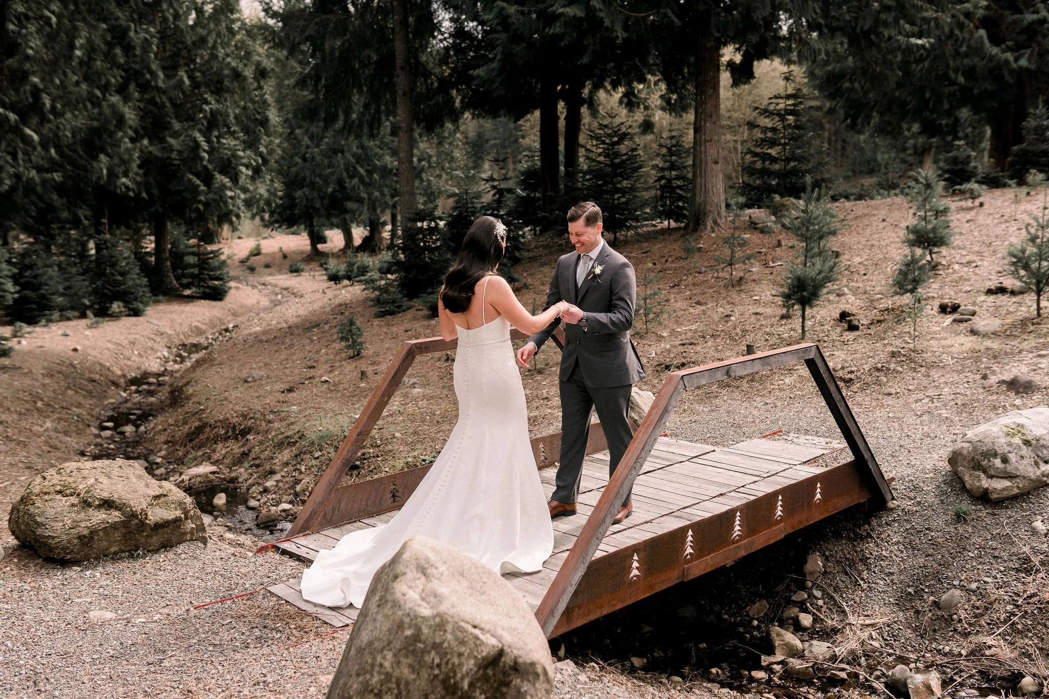 A bride and groom exchanging vows on a small wooden bridge in a forested area.