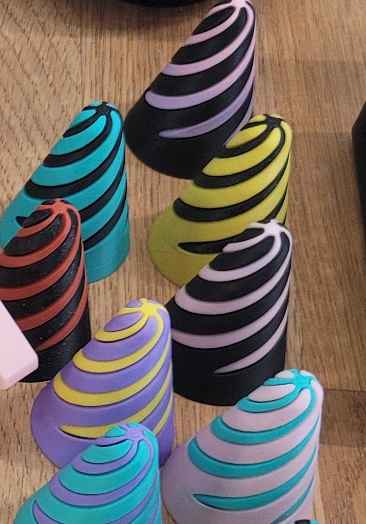 Colorful cone-shaped objects with swirl patterns in various colors including pink, purple, yellow, turquoise, orange, and black, arranged on a wooden surface.