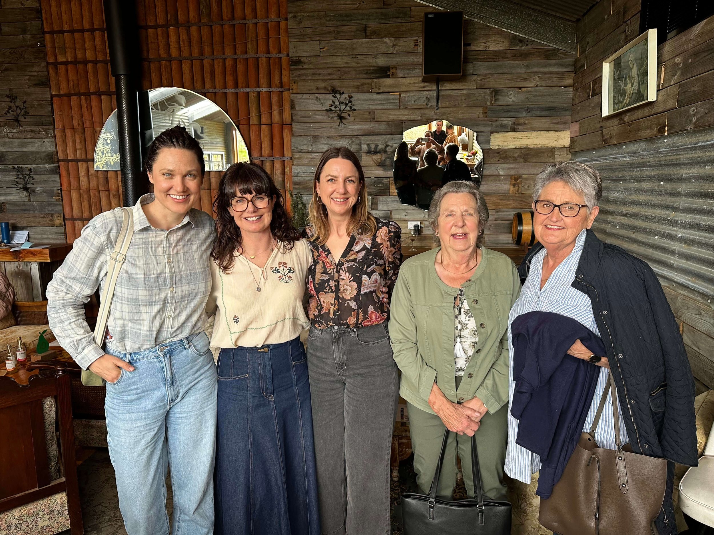 Five women standing together in a cozy, rustic wooden room, smiling at the camera.