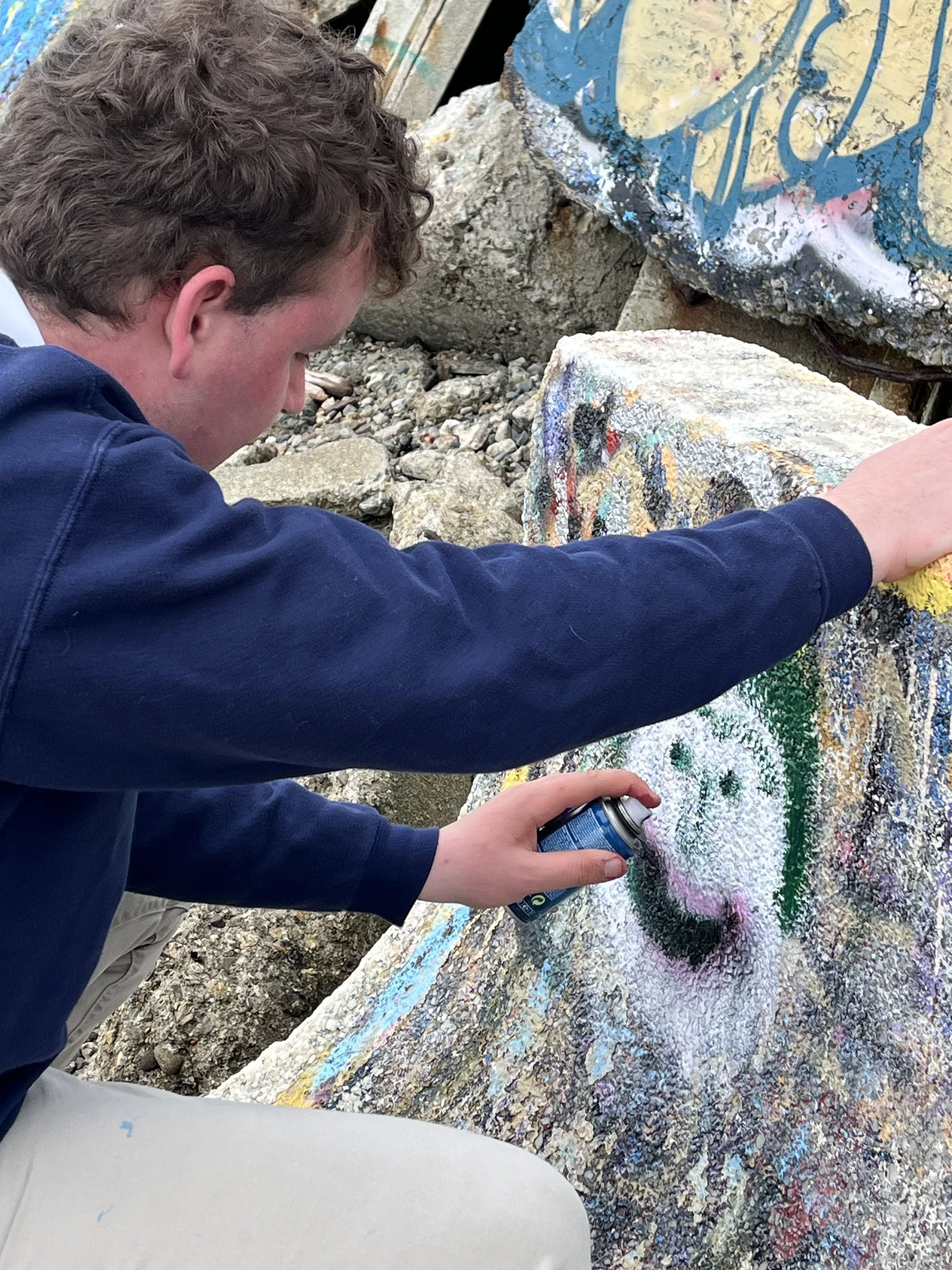 A person spray painting a colorful design on a large rock.