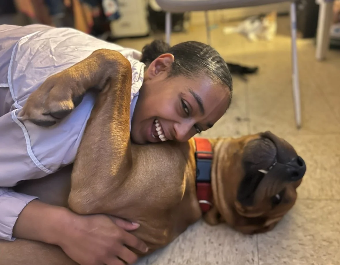 A young woman hugging a large, brown dog lying on the floor, both smiling.
