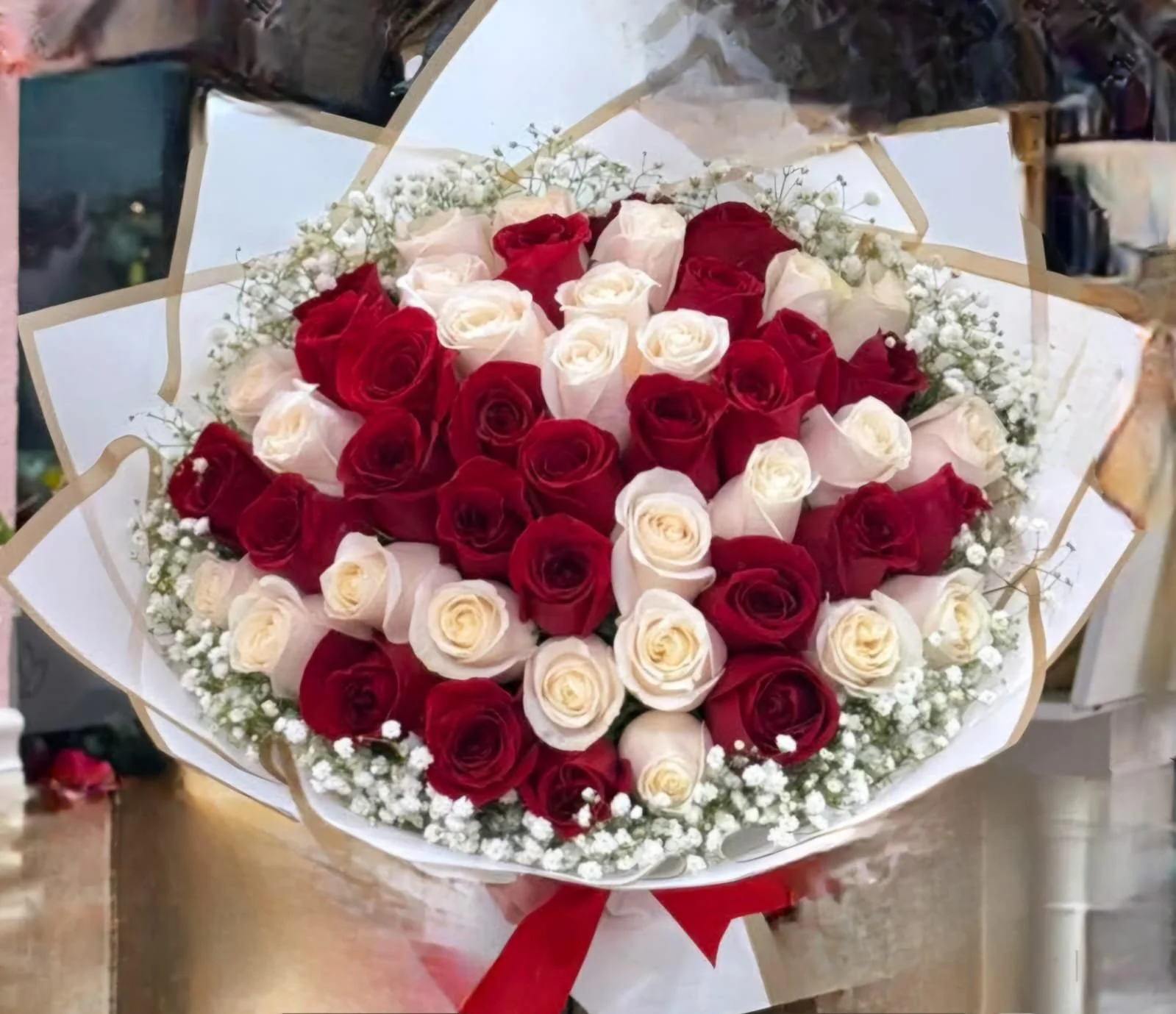 A bouquet of red and white roses wrapped in decorative paper with baby's breath flowers, tied with a red ribbon.