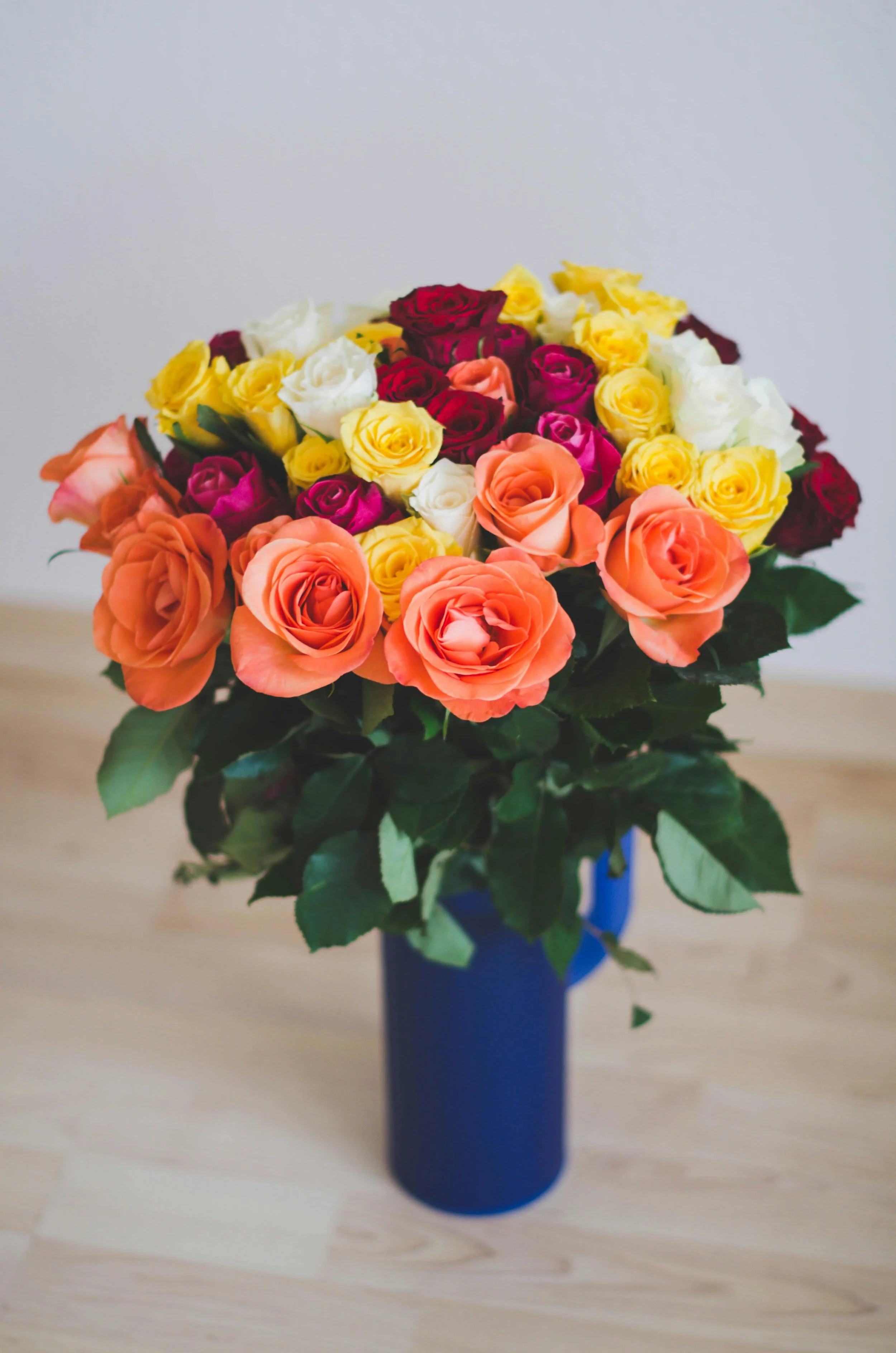 A bouquet of multicolored roses in a blue vase on a wooden surface.