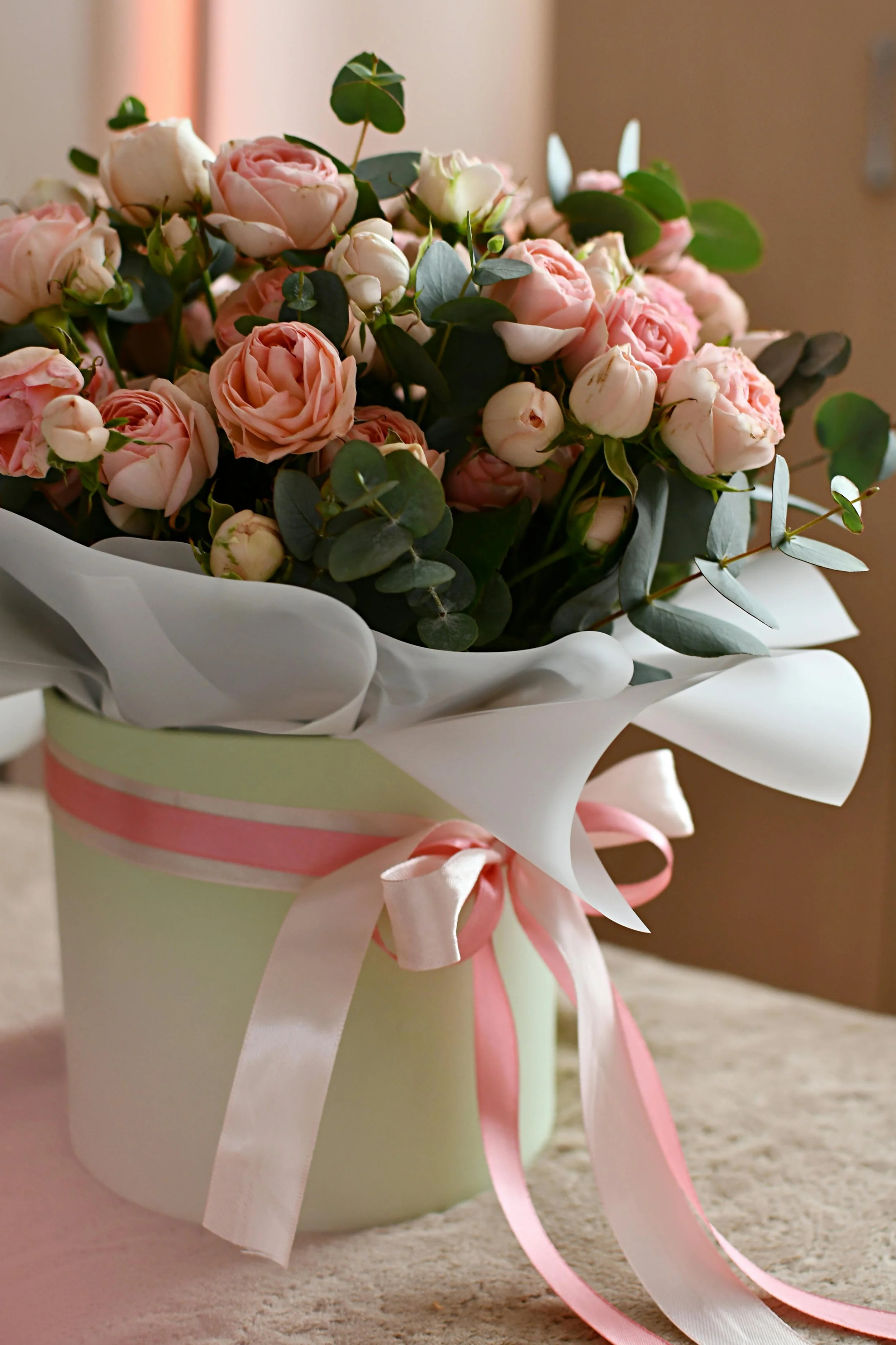 A bouquet of pink roses and white roses with green leaves in a light green gift box wrapped with white and pink ribbons.